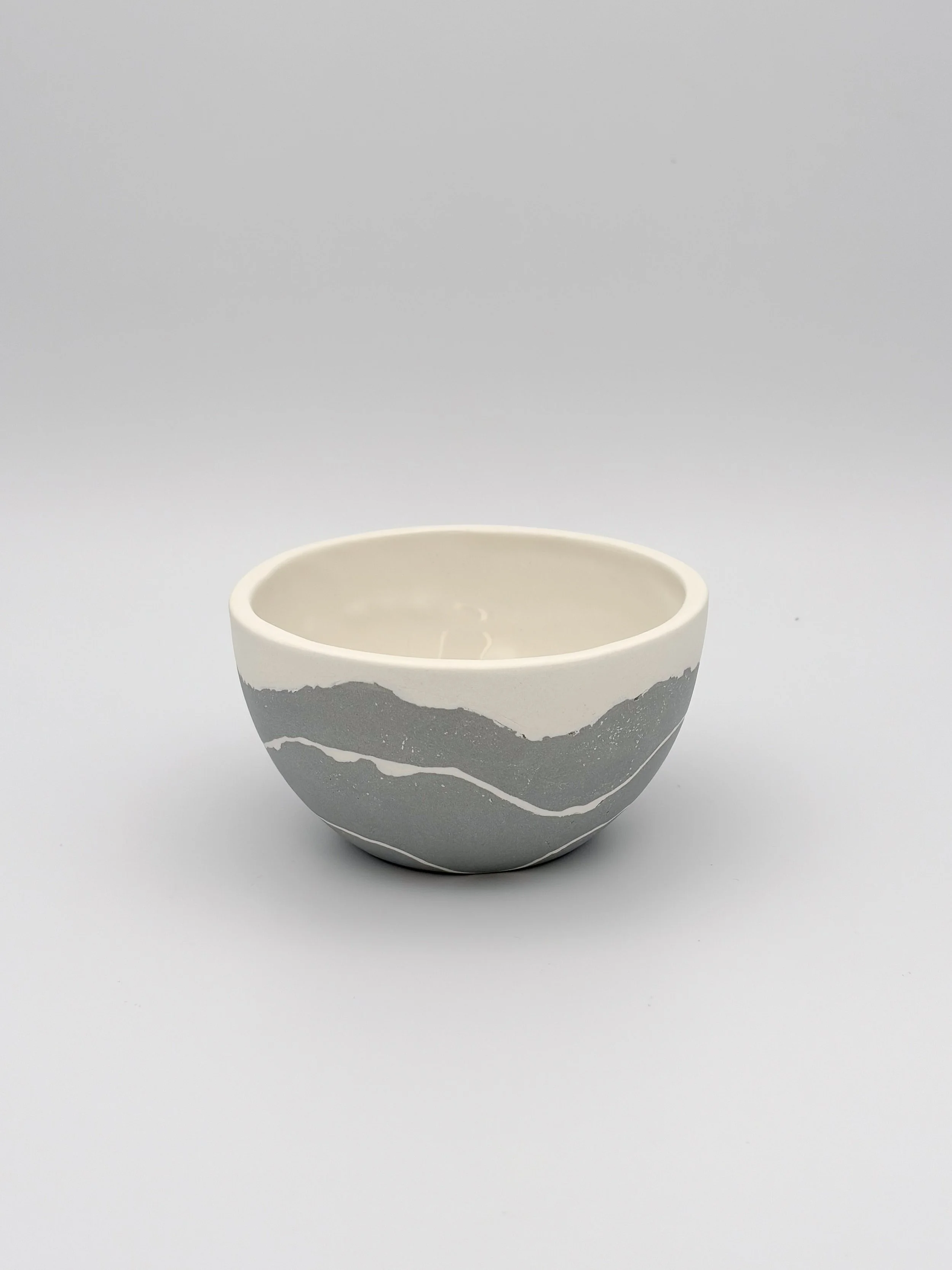 A white ceramic bowl with a mountain landscape design in gray, featuring jagged peaks and layered slopes, on a plain white surface.