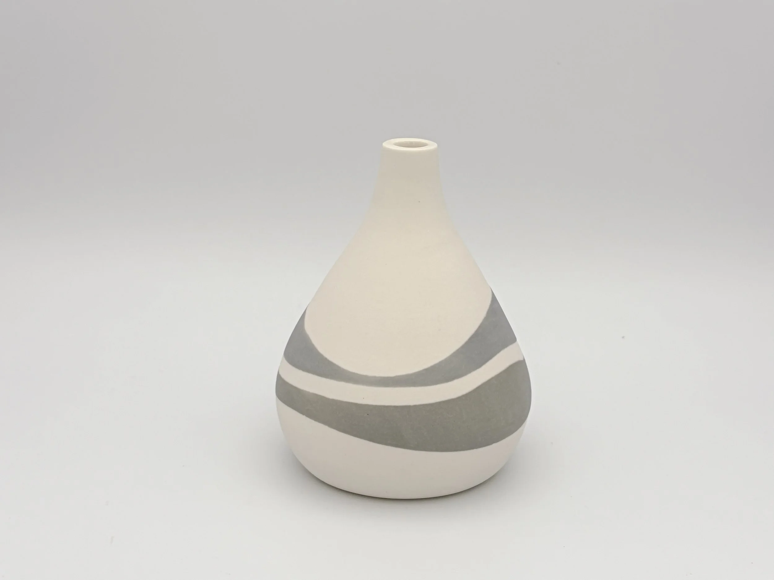 A white ceramic vase with black and gray spiral patterns, photographed against a plain grey background.