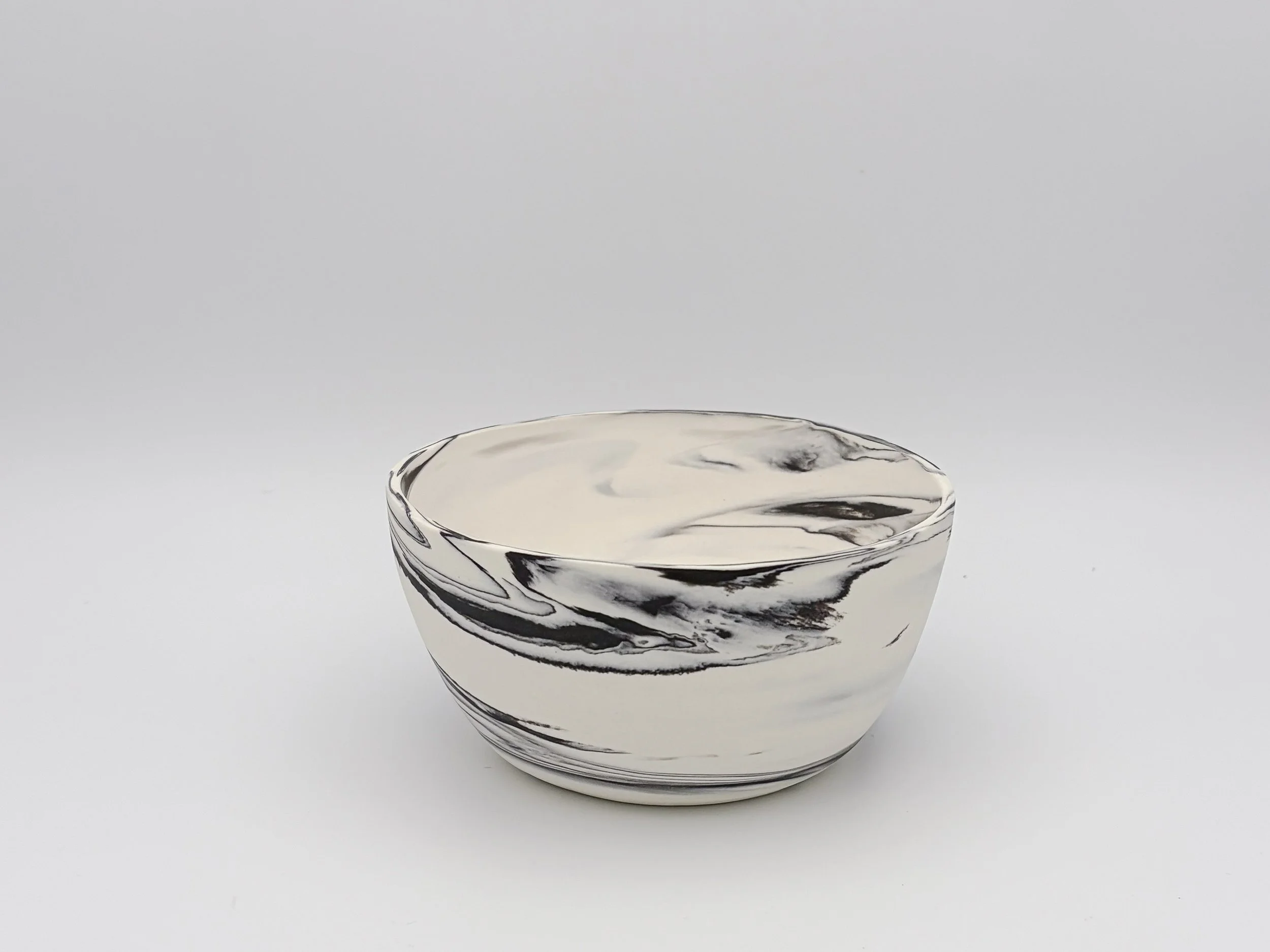 A small ceramic bowl with a black and white marble pattern, placed on a white background.