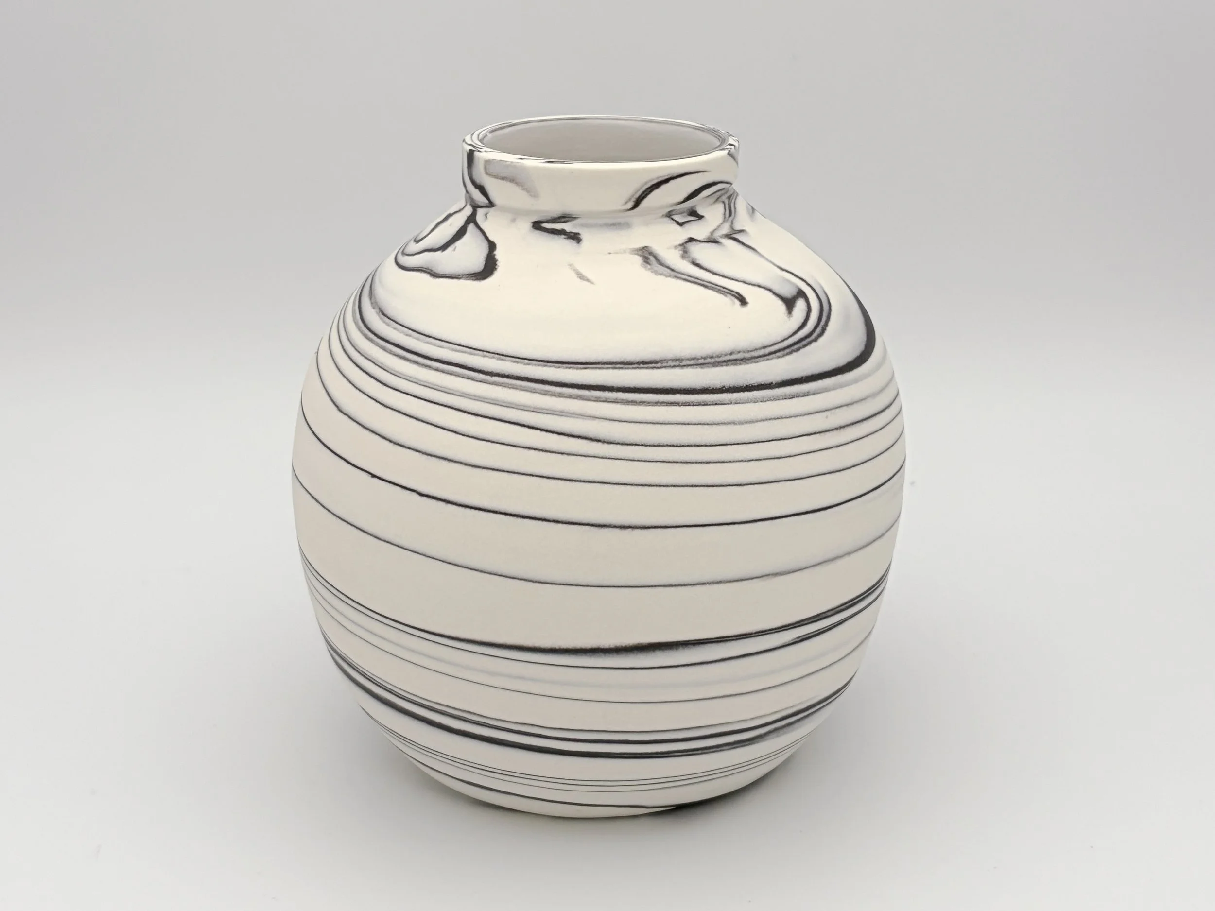 A white ceramic vase with black swirling lines, featuring a narrow opening and a rounded body, set against a plain light background.
