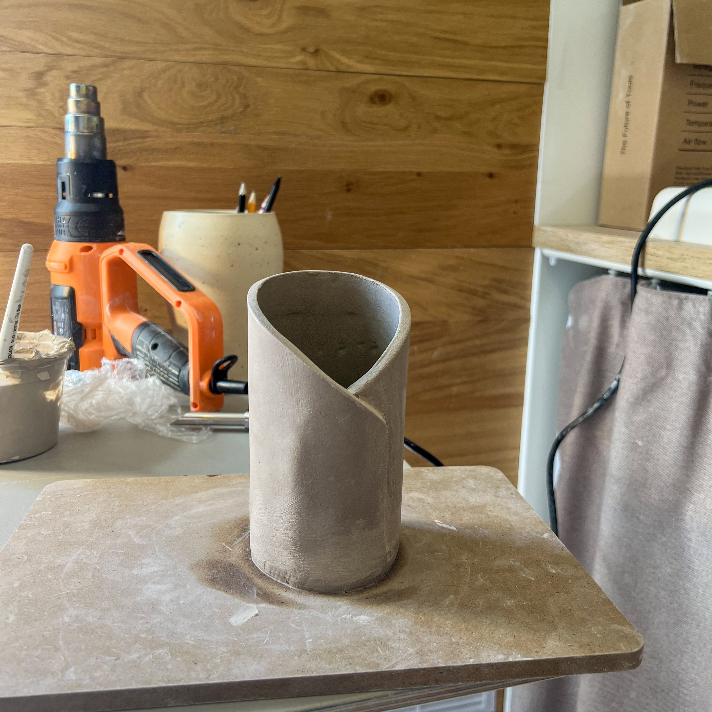 A cylindrical ceramic vase with a modern twisted design on a table in a pottery studio.