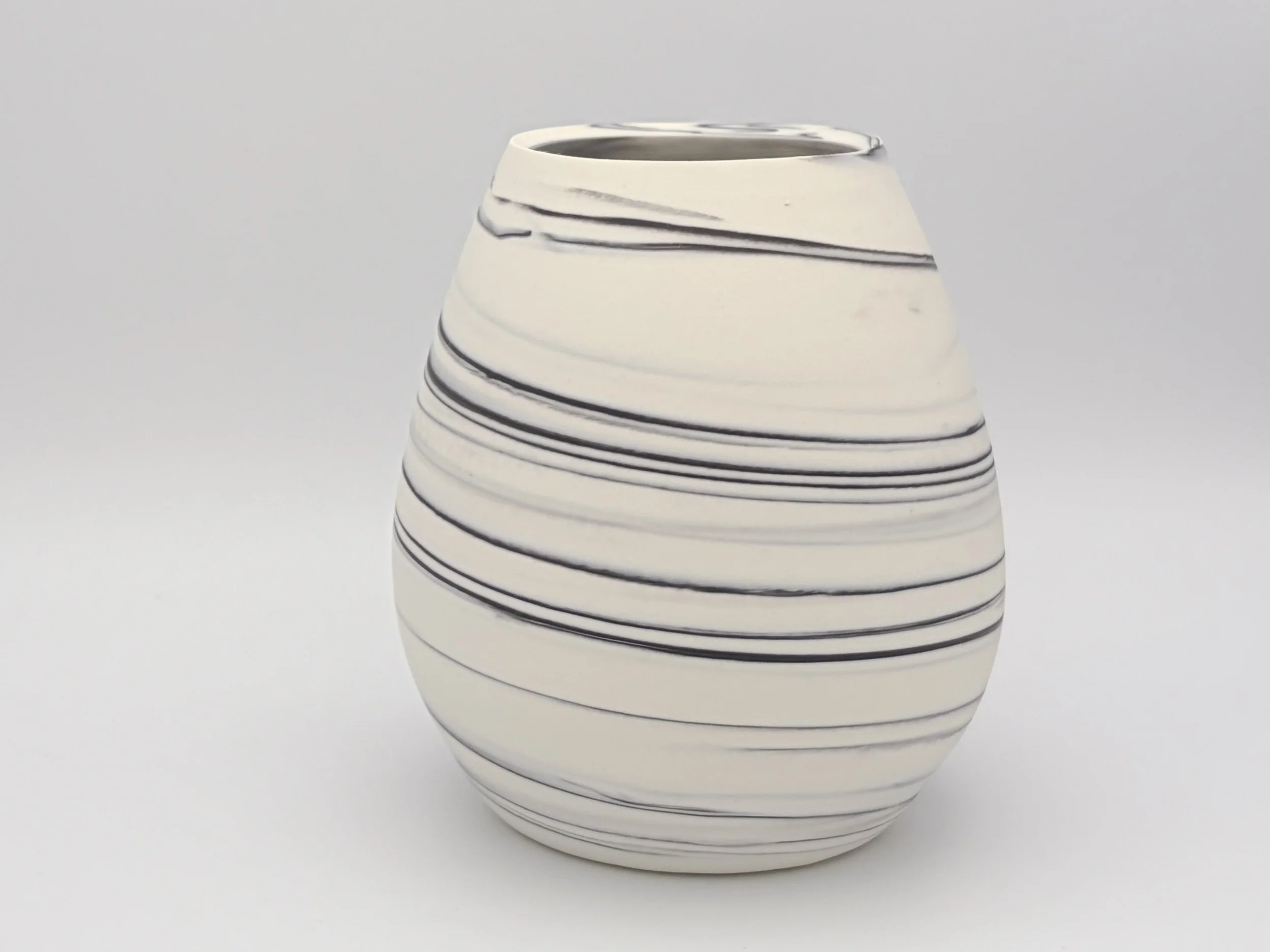 A white ceramic vase with black horizontal swirl lines, set against a plain light background.