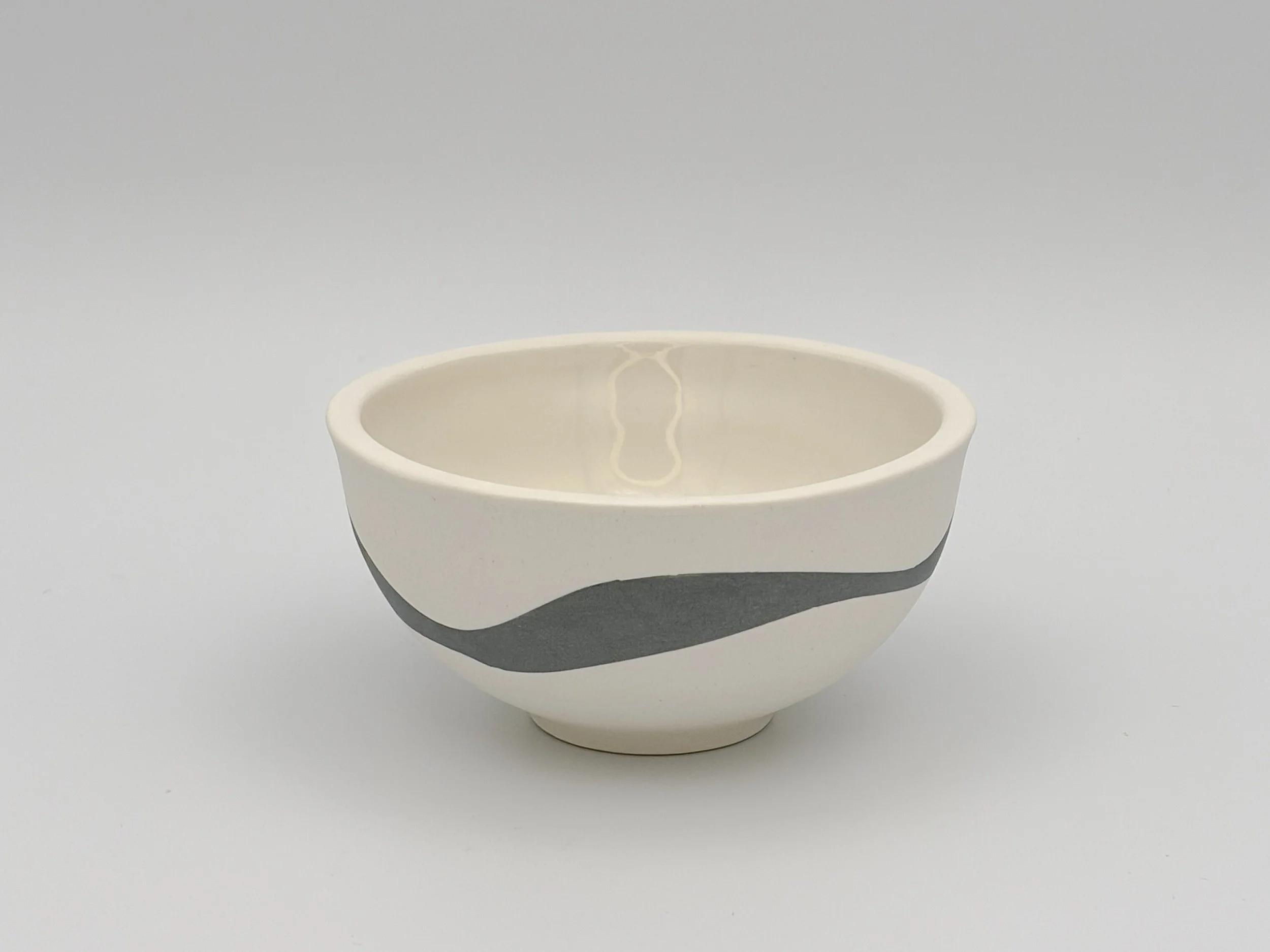 A plain white porcelain bowl with a blue slip design, set against a light grey background.