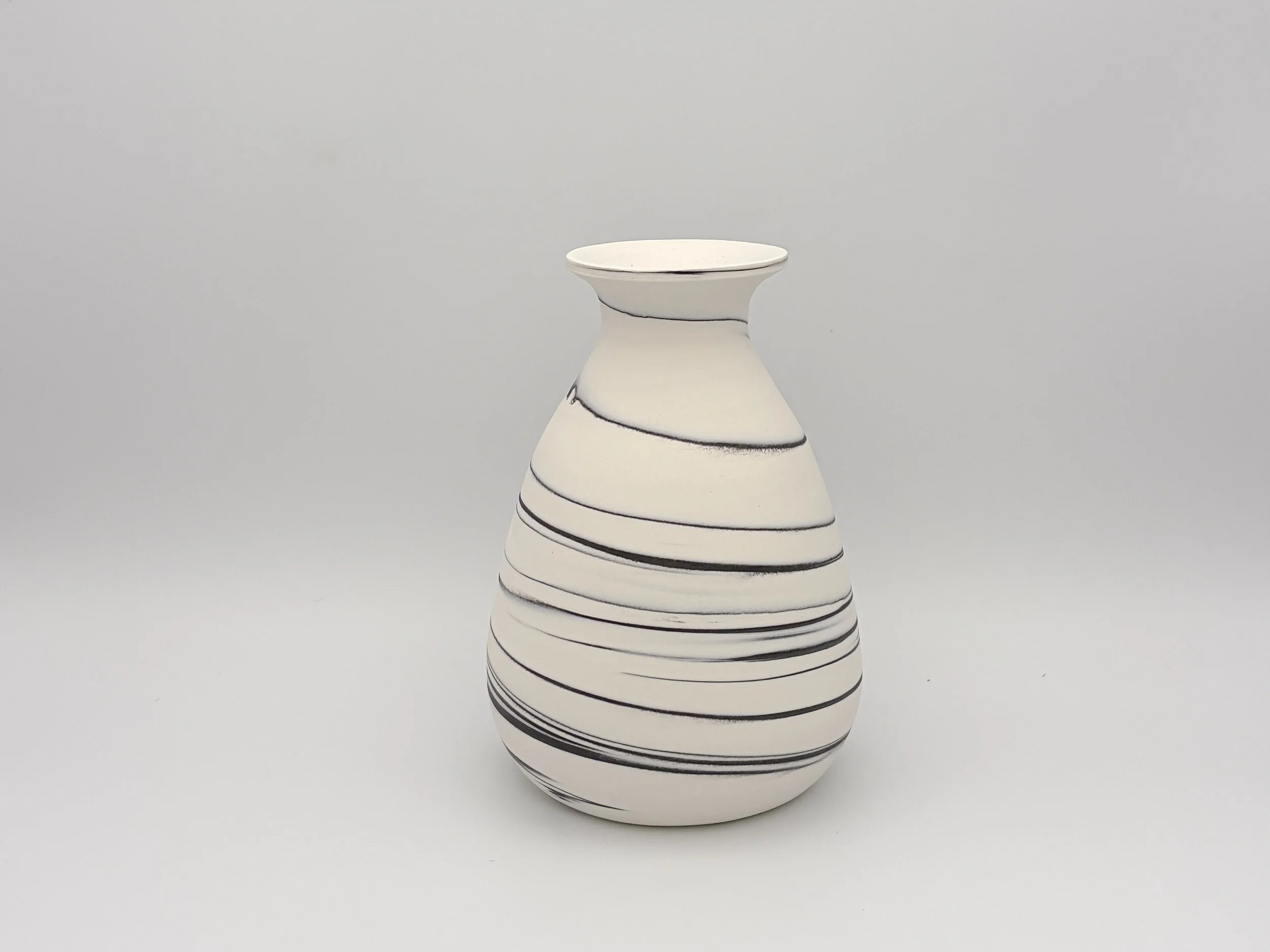 A white ceramic vase with black spiral lines, placed against a plain gray background.