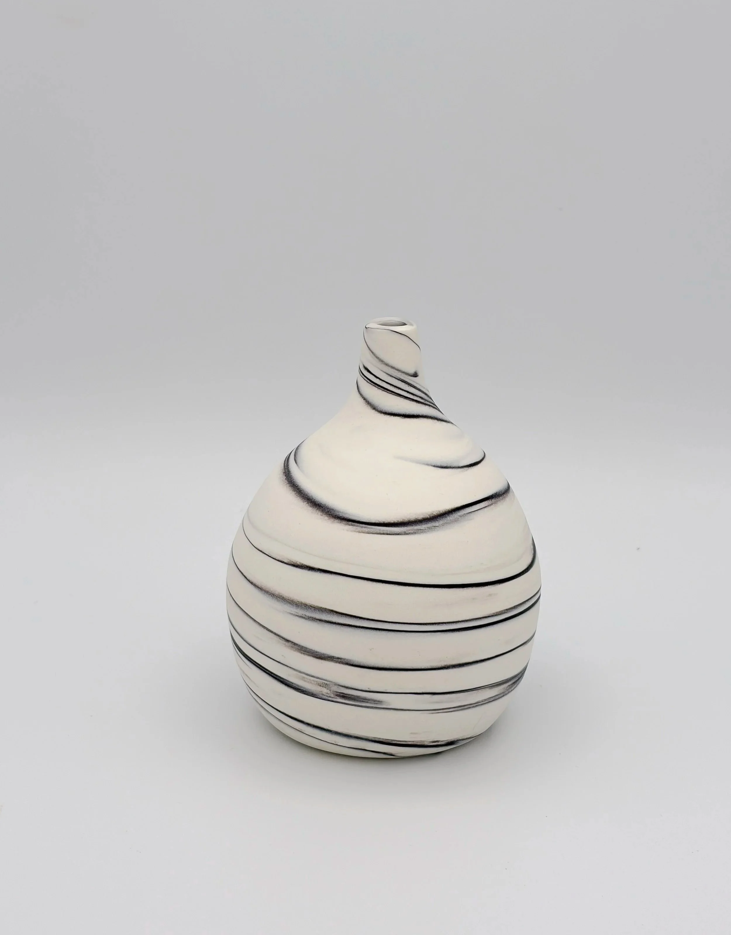 A white ceramic vase with black swirling lines and black horizontal stripes, set against a plain, light gray background.