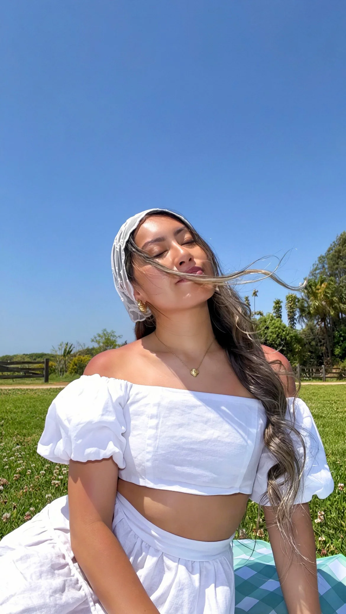 Radiant woman sitting in a green field, drinking in the sunshine