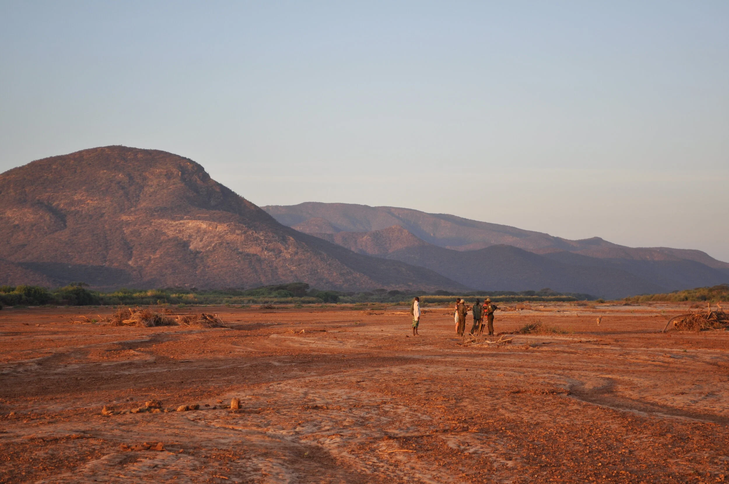 Travellers on walking safari through the expansive landscapes of northern Kenya beneath distant mountain ranges.