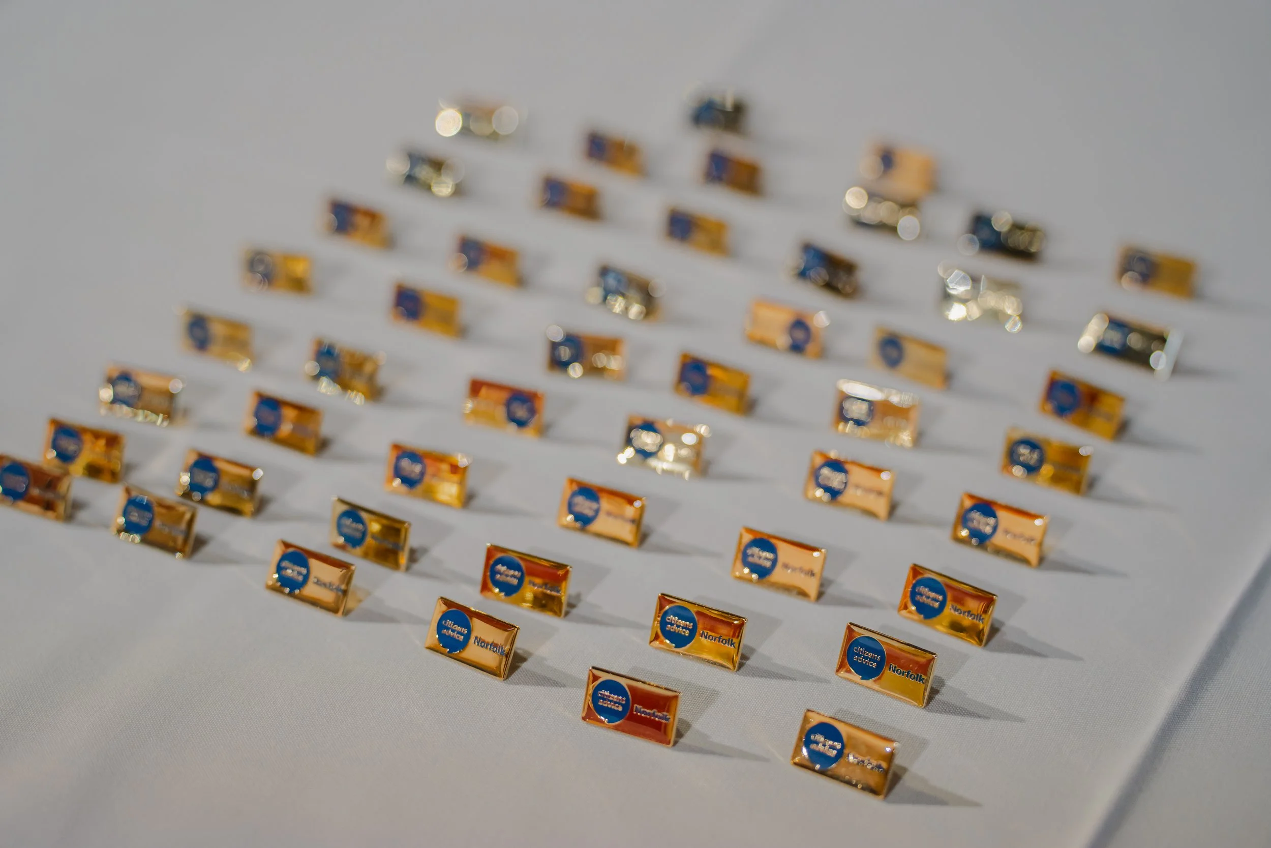 Gold Norfolk Citizens Advice Badges sitting on a white tablecloth