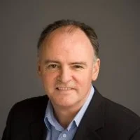 Professional headshot of a middle-aged man wearing a dark blazer and light blue shirt against a neutral background.