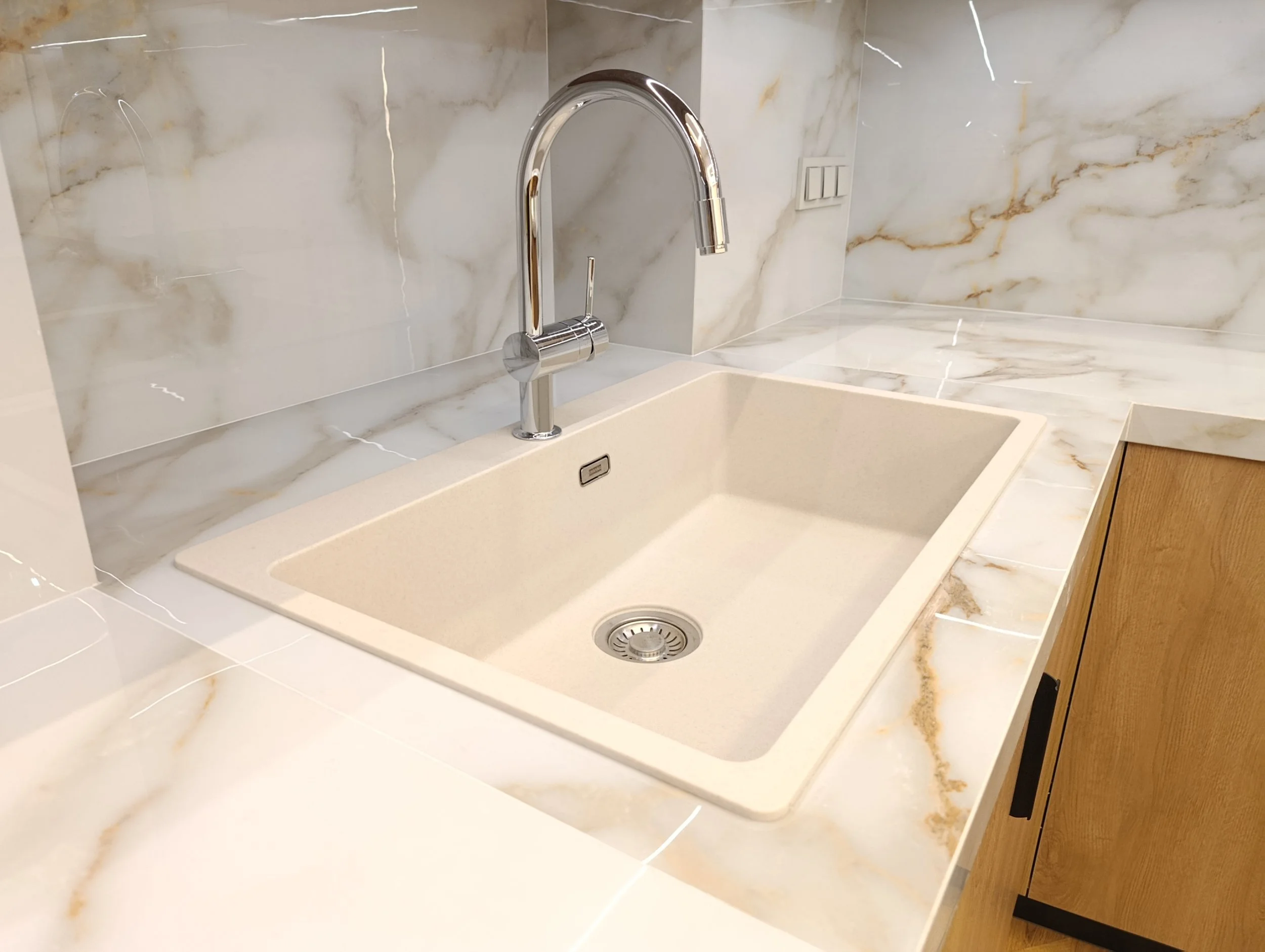 Kitchen sink with beige basin, stainless steel faucet, marble backsplash, and marble countertop.