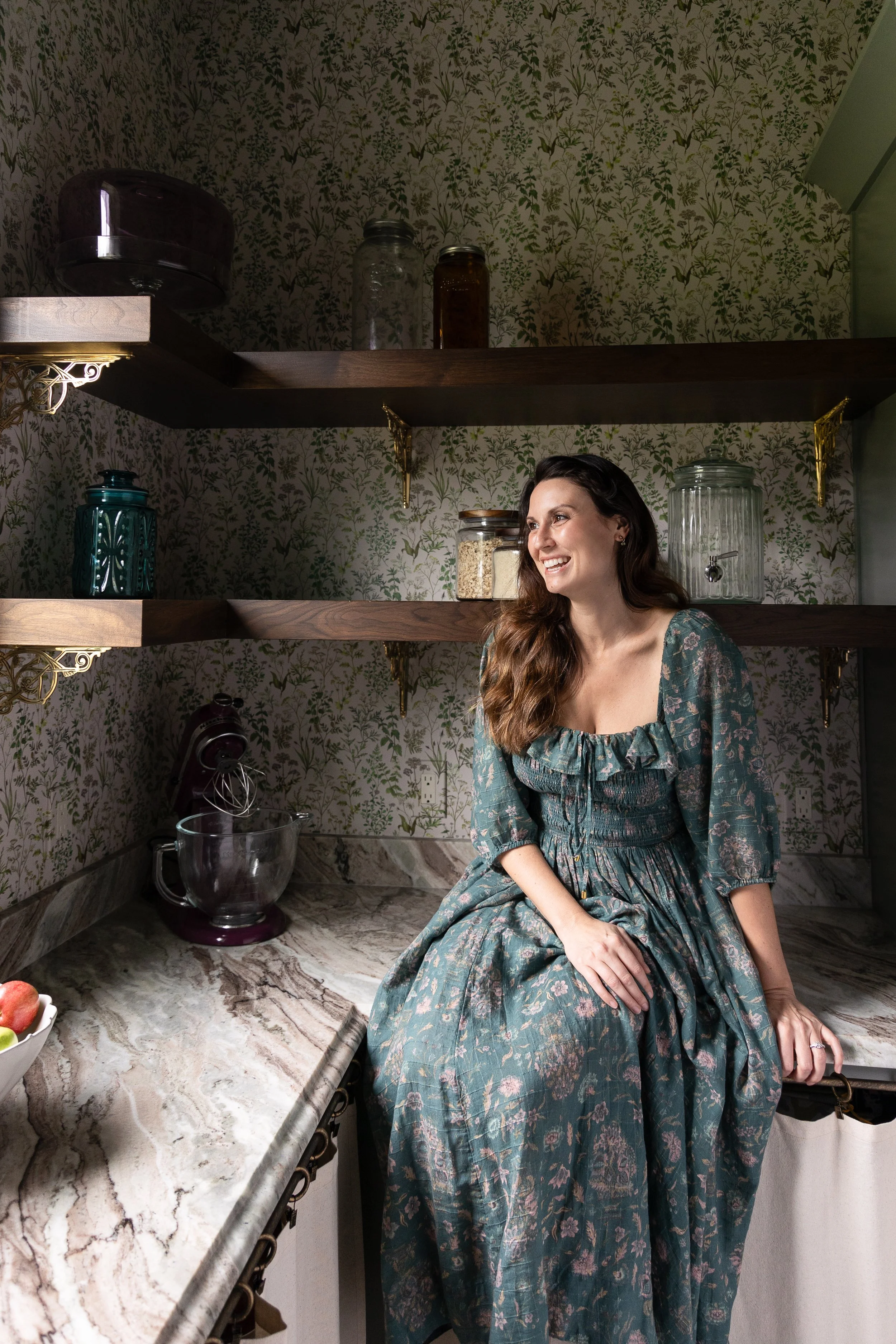 Austin interior designer Anne Barger standing in a beautifully appointed kitchen wearing a floral dress, showcasing her signature warmth and refined design aesthetic