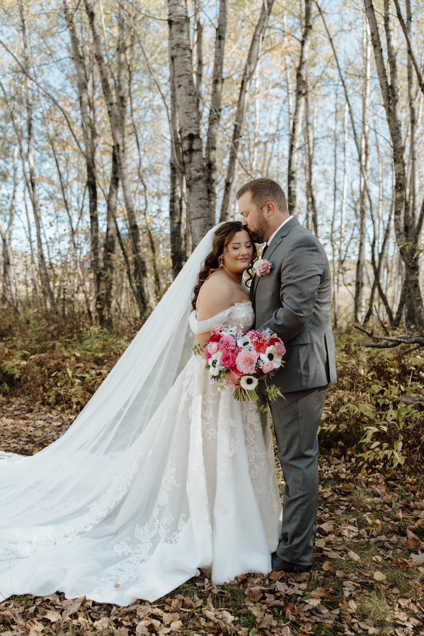 Wedding couple posing, bride with her assorted pinks bouquet and groom with pocket square boutonniere flowers designed by For Floral Sake in Duluth, Minnesota