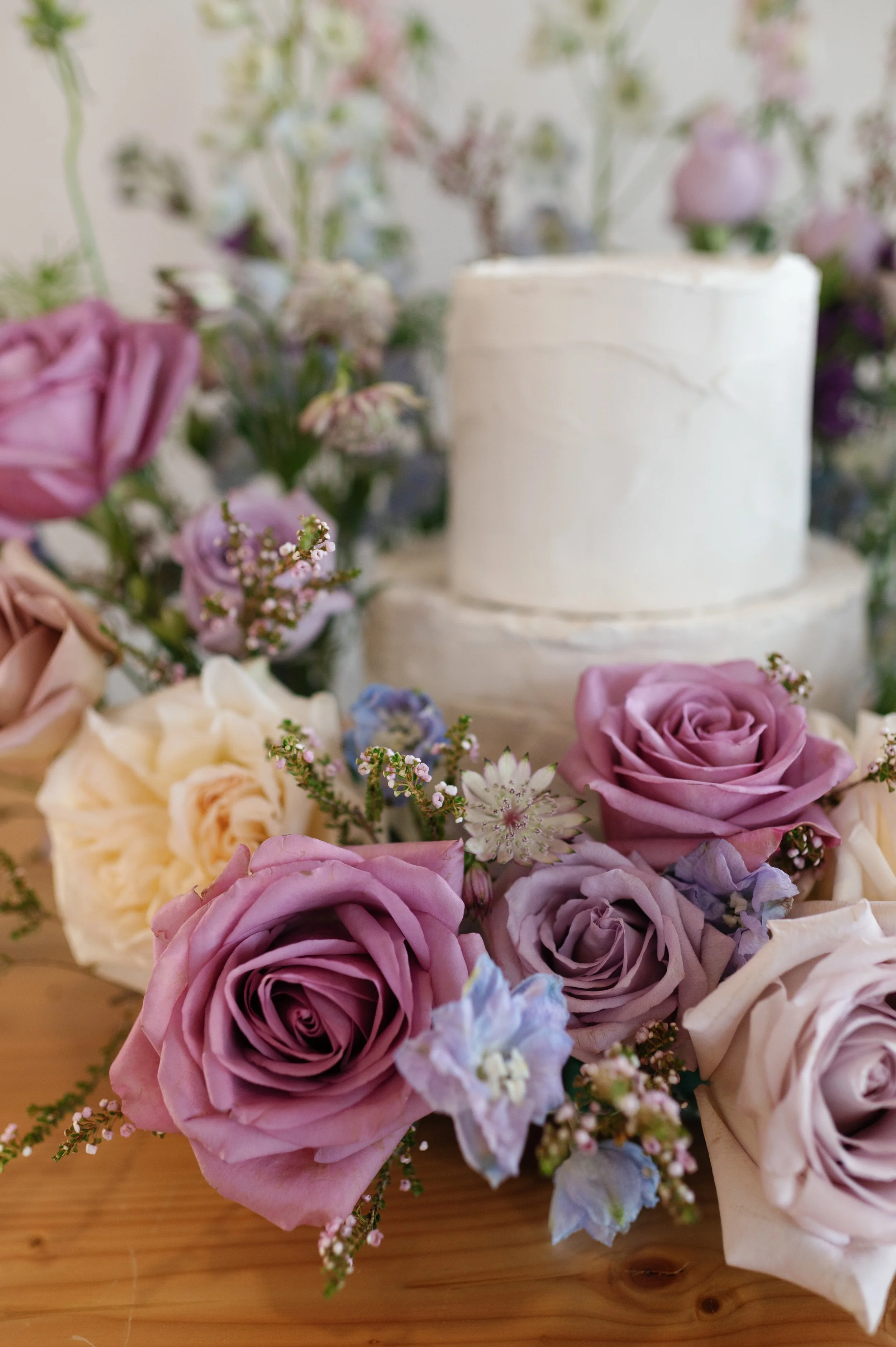 A whimsical floral meadow of purples, blush, and lavender blooms surrounding a two-tiered wedding cake. Designed by a Duluth, MN luxury wedding florist, this floral styling creates a lush, romantic centerpiece perfect for modern, garden-inspired wedd