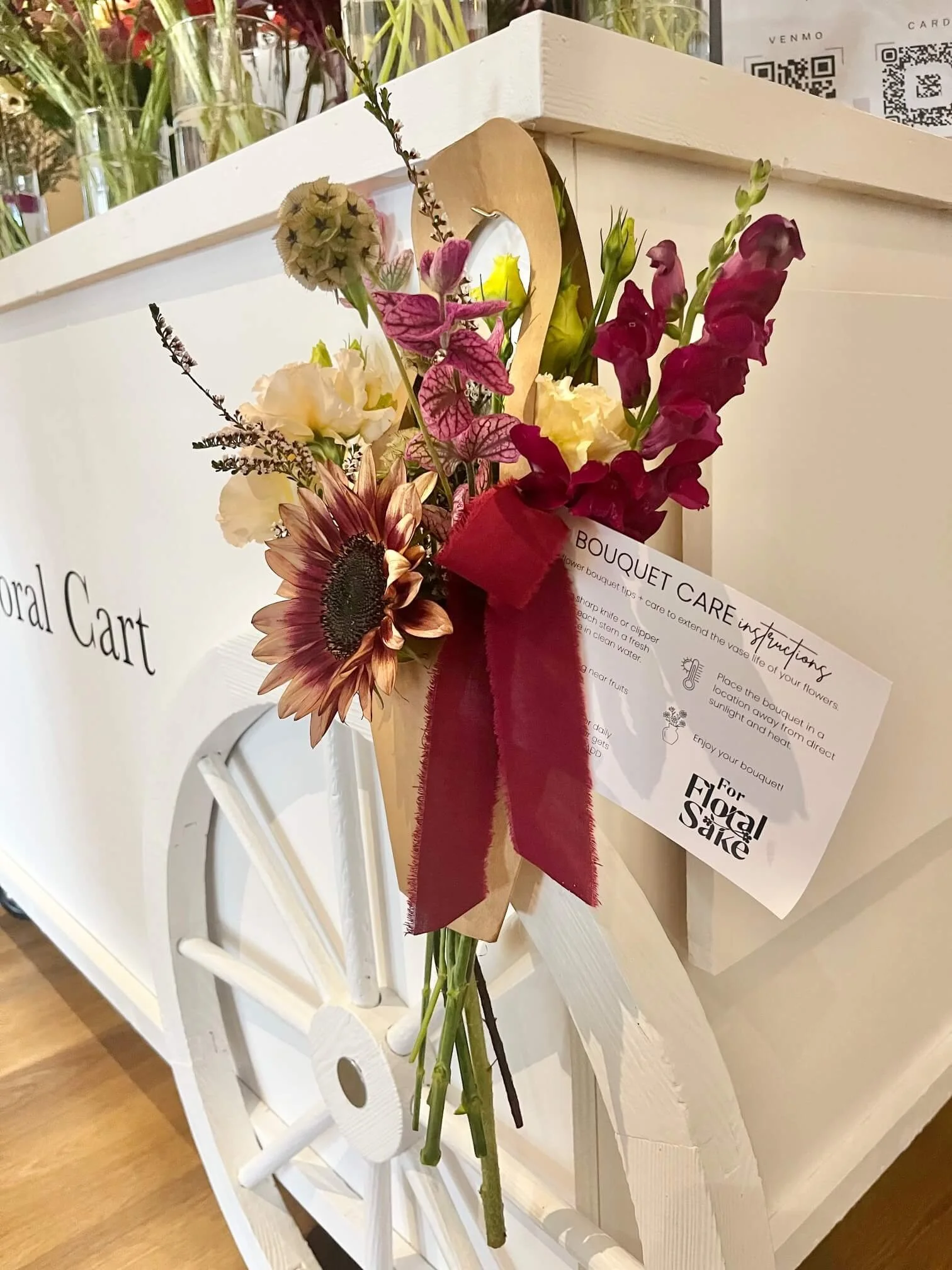 Pre-made hand-wrapped bouquet created from late summer blooms next to a wagon wheel floral cart.