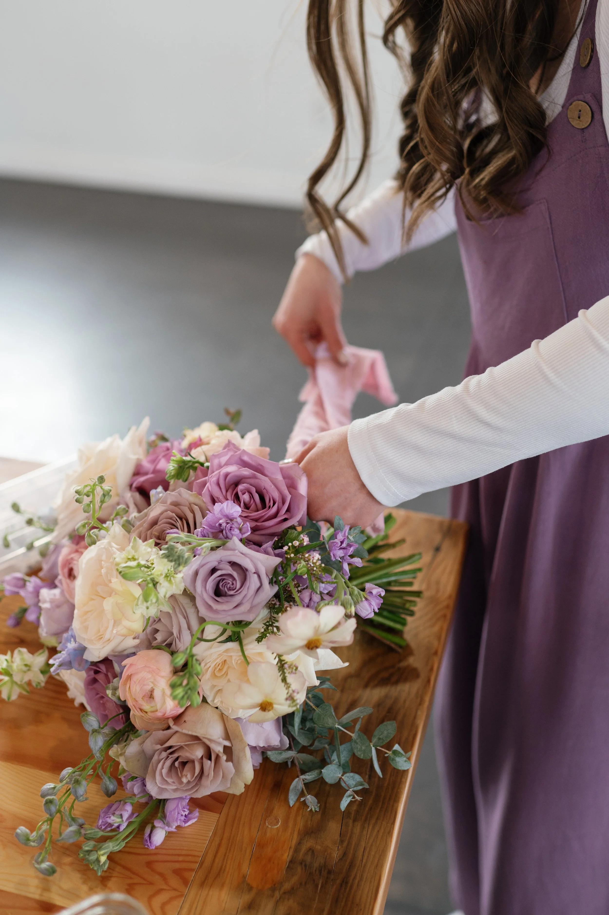 A wedding florist in Duluth, MN ties soft silk ribbons to a romantic bridal bouquet in hues of lavender and blush. A refined, artistic touch showcasing the attention to detail and elegance of full-service luxury floral design.