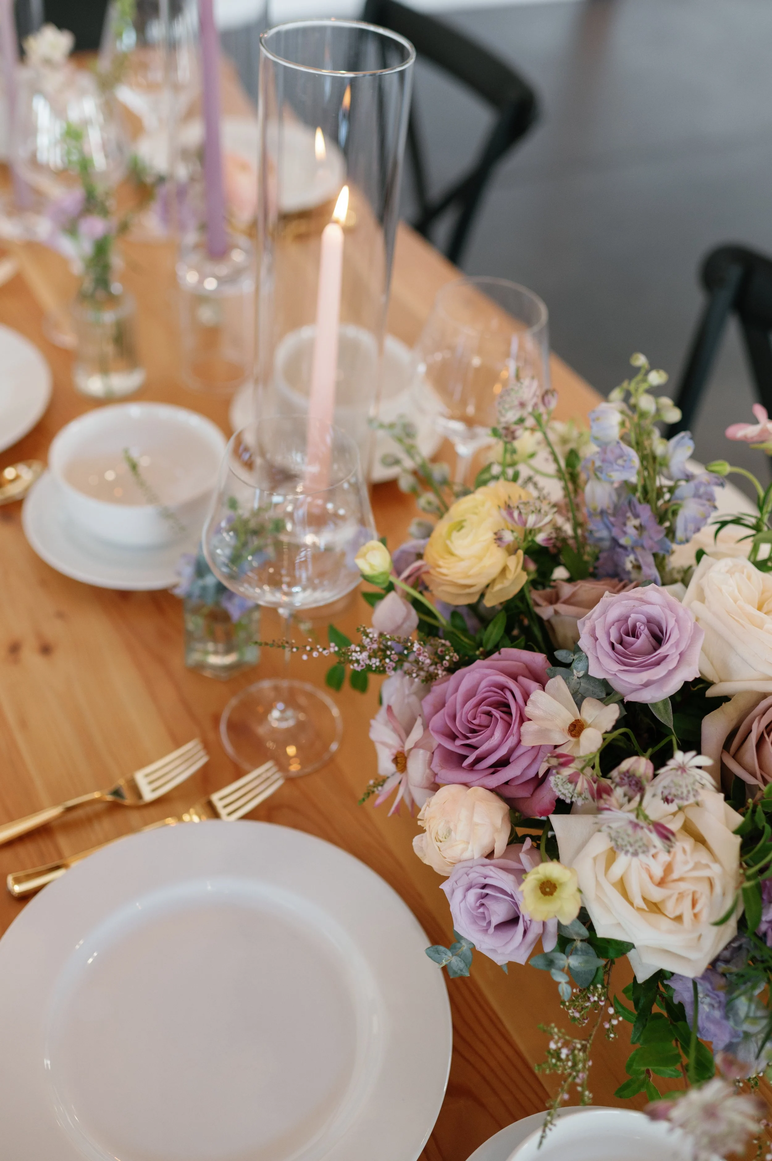 An elegant wedding tablescape featuring a lush centerpiece of purple and blush florals accented by taper candles. Designed by a Duluth, MN wedding florist specializing in luxury full-service floral design for timeless, romantic celebrations.