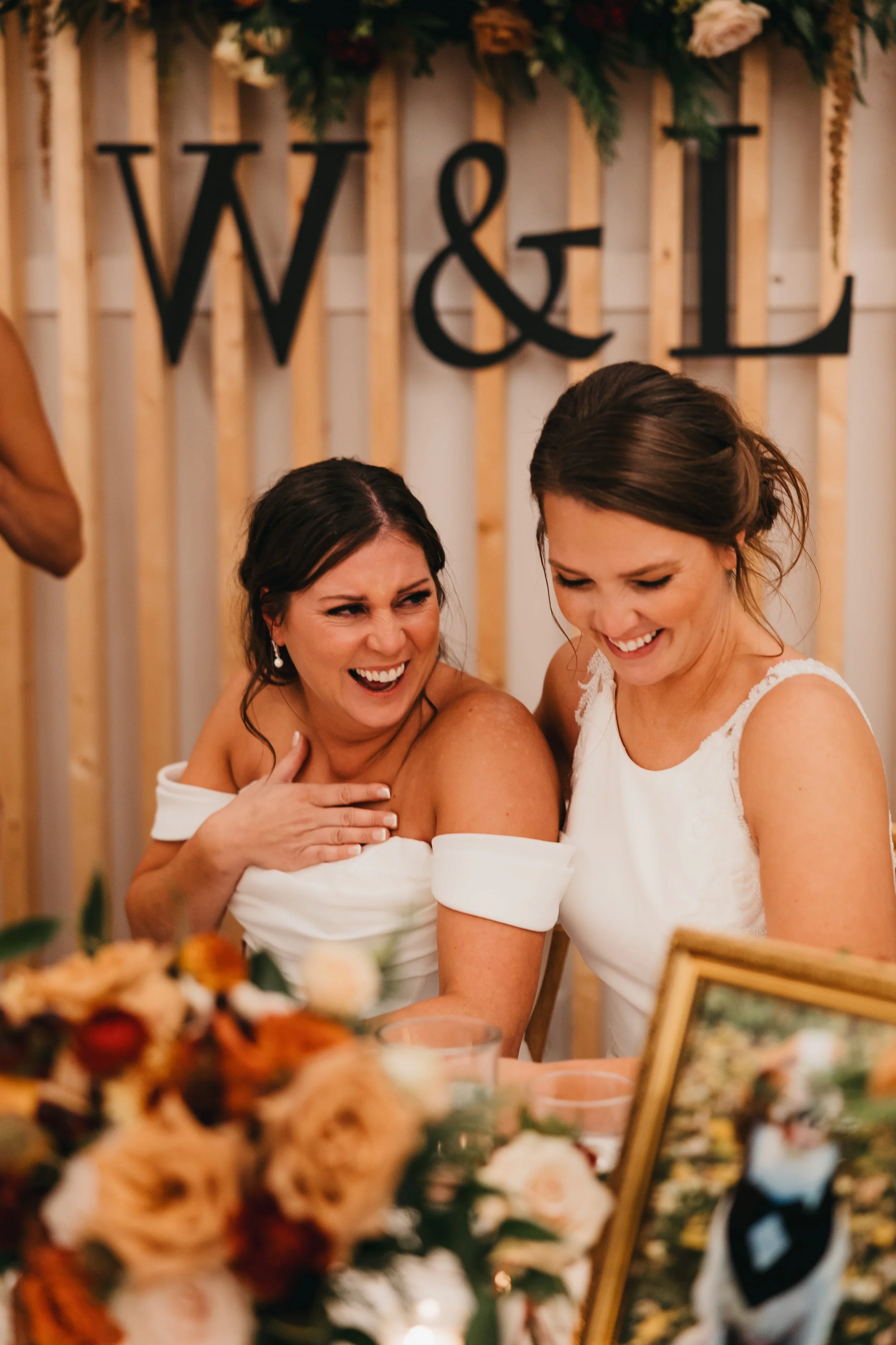 Two brides laughing together while seated at the head table at a Nisswa wedding.