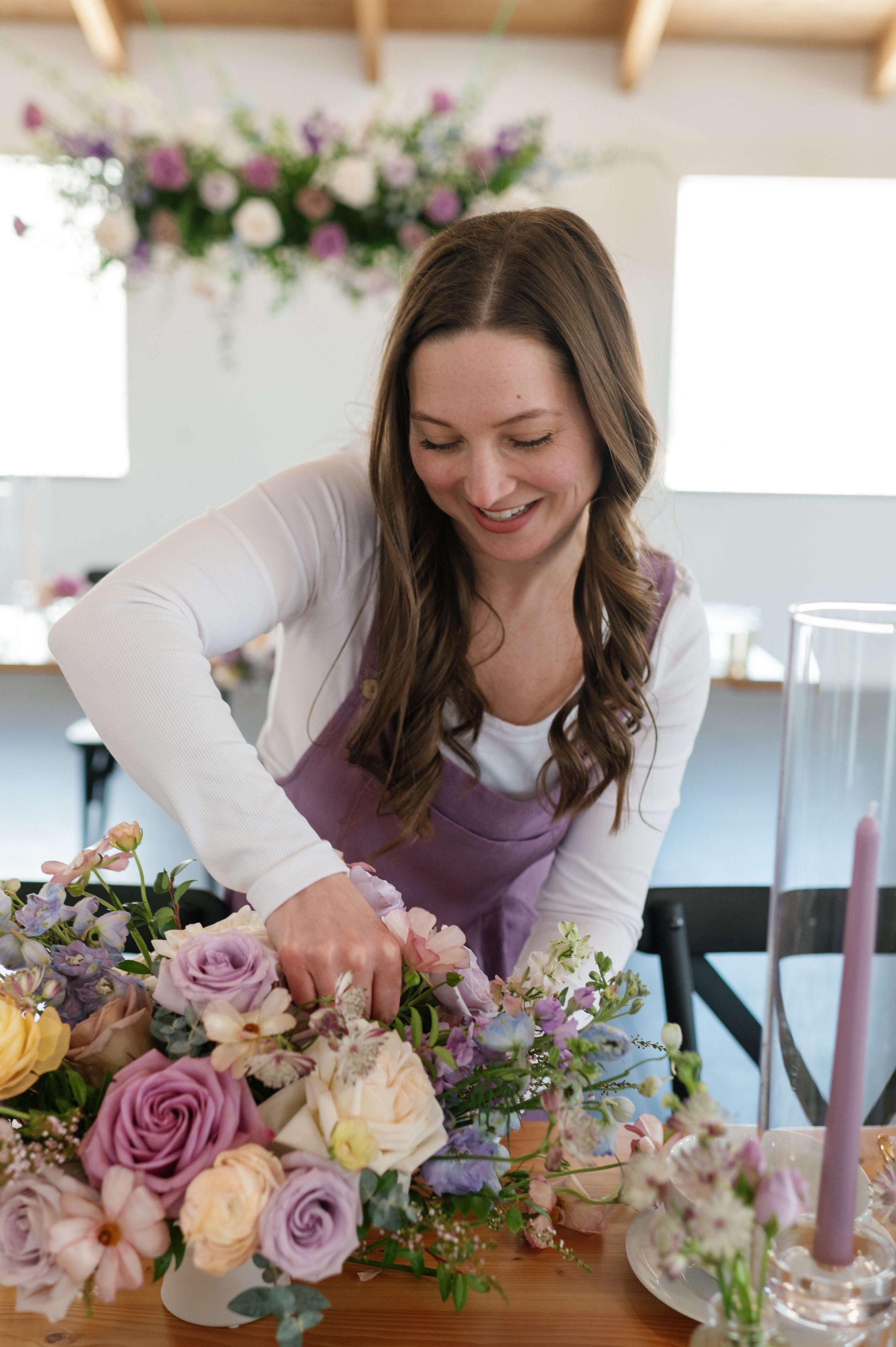 For Floral Sake florist adjusting a floral wedding centerpiece with a suspended floral installation in the background.