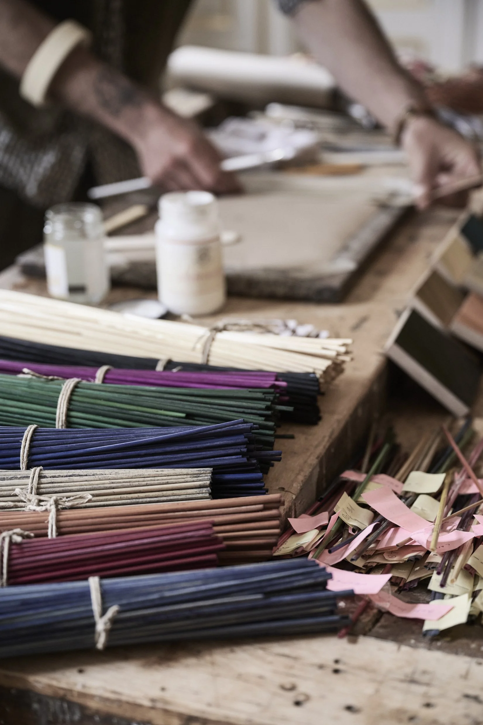Colorful bundles of incense sticks and small jars on a wooden surface in a workshop.