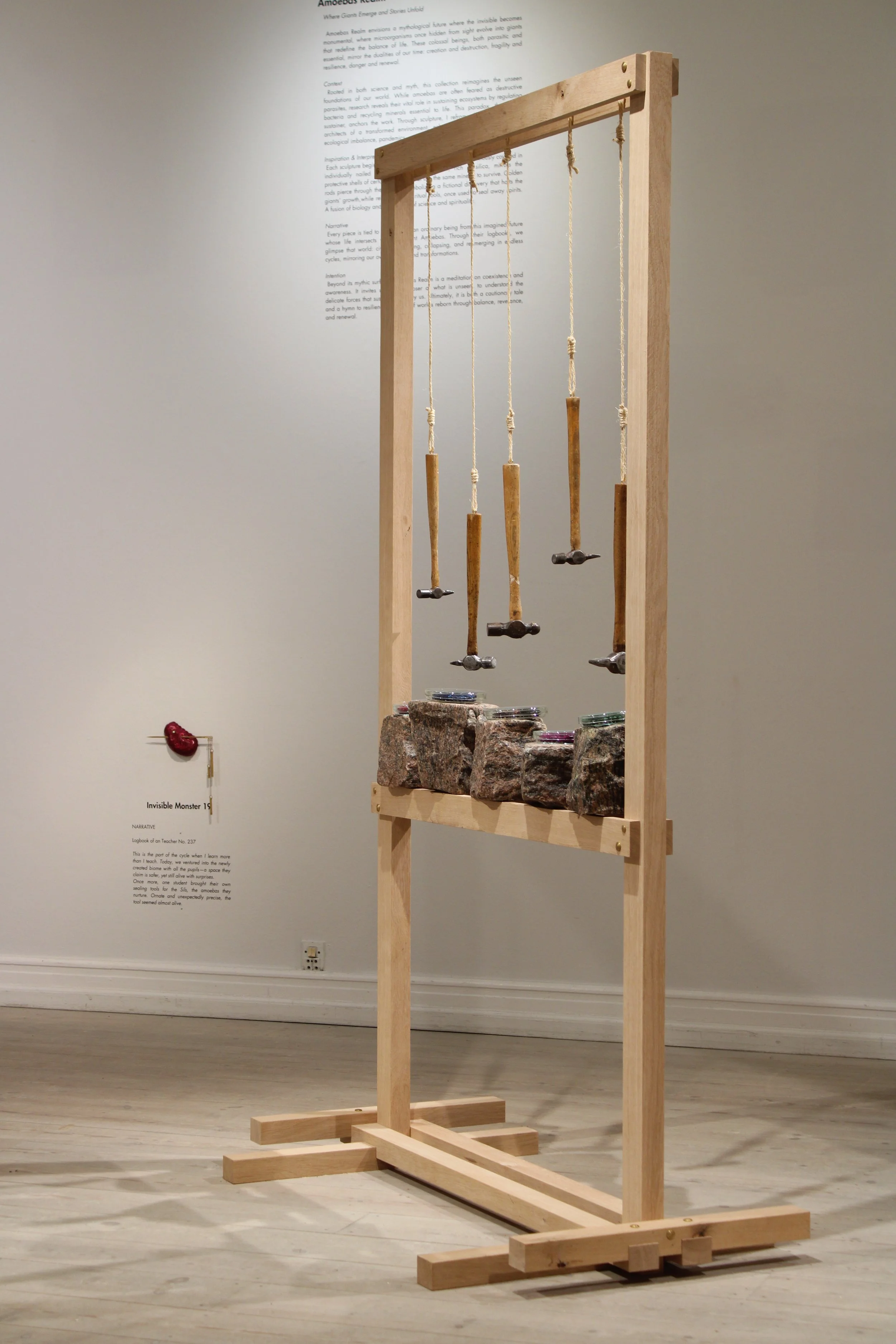 Invisible monster 22 by Jonathän Jouan Studios, Amoebas Realm collection. Contemporary art installation  wood stone and suspended hammer. Petri dishes with microorganism representation in rye straw marquetry in it.