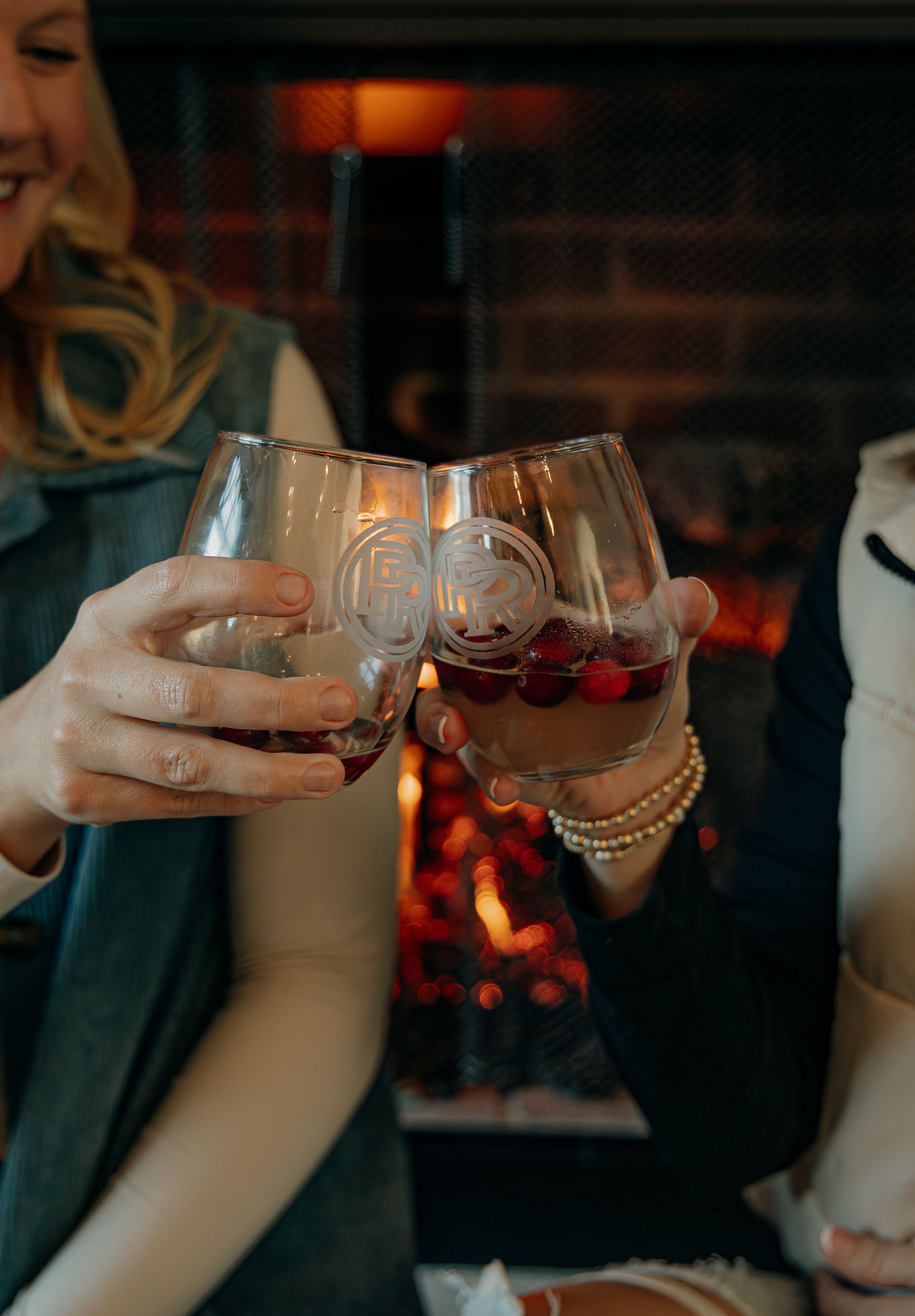 Two women clinking glasses with red wine and cherries in a cozy, warm setting.
