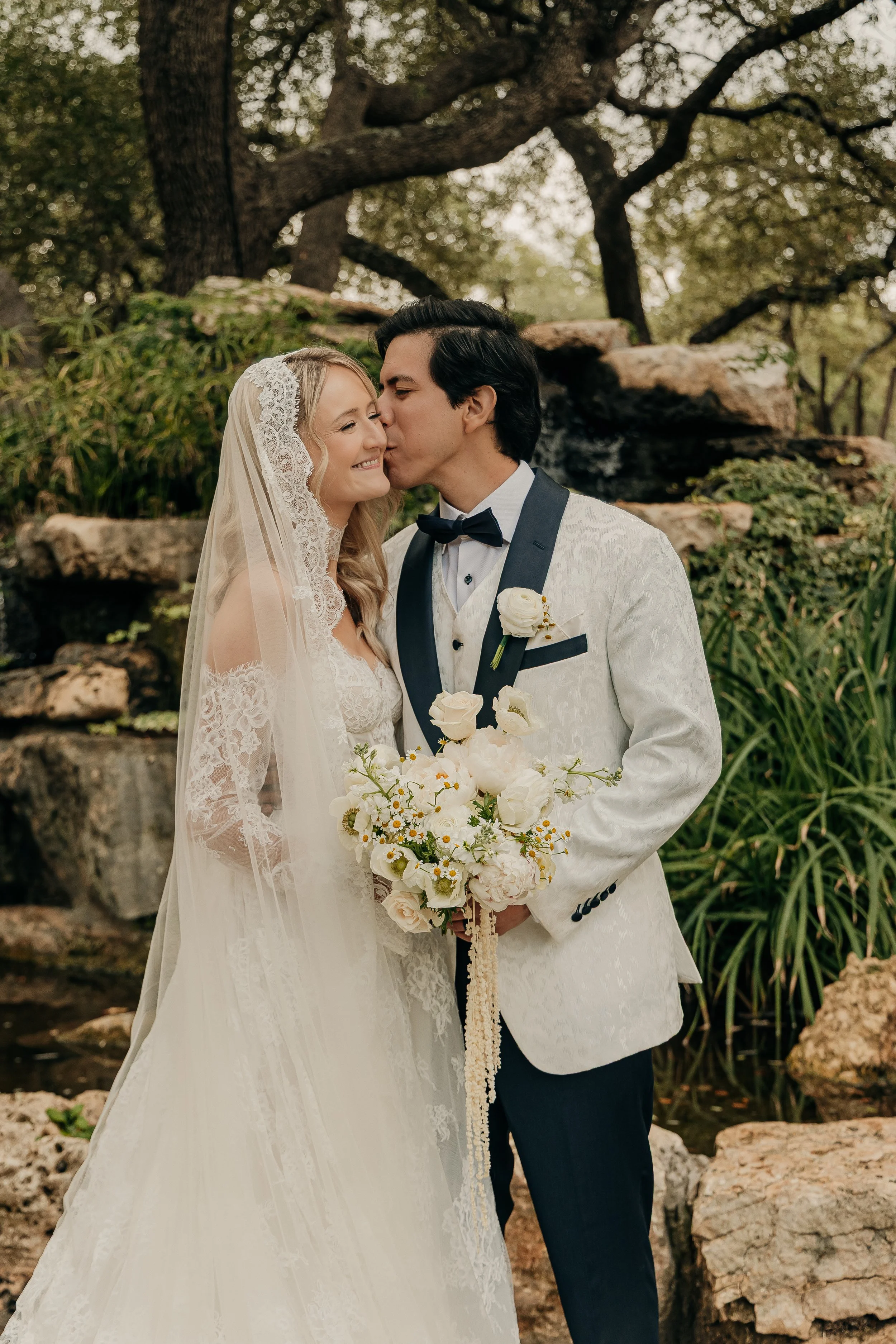 Bride and groom sharing a kiss outdoors during their wedding, with natural greenery and rocks in the background.