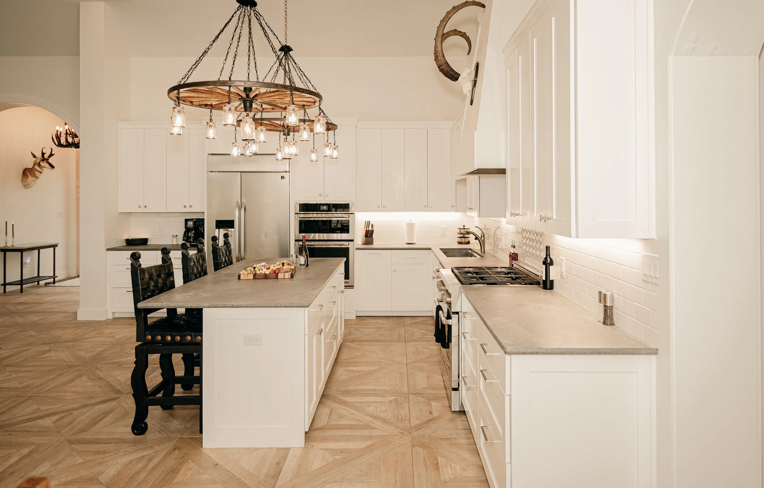 Modern kitchen with white cabinets, a large island with black chairs, and a chandelier with multiple Mason jar-style lights.
