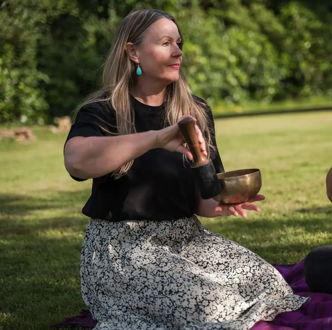 Gillian Campbell, Glasgow yoga teacher trainer, holding a singing bowl outdoors in a calm, natural setting.