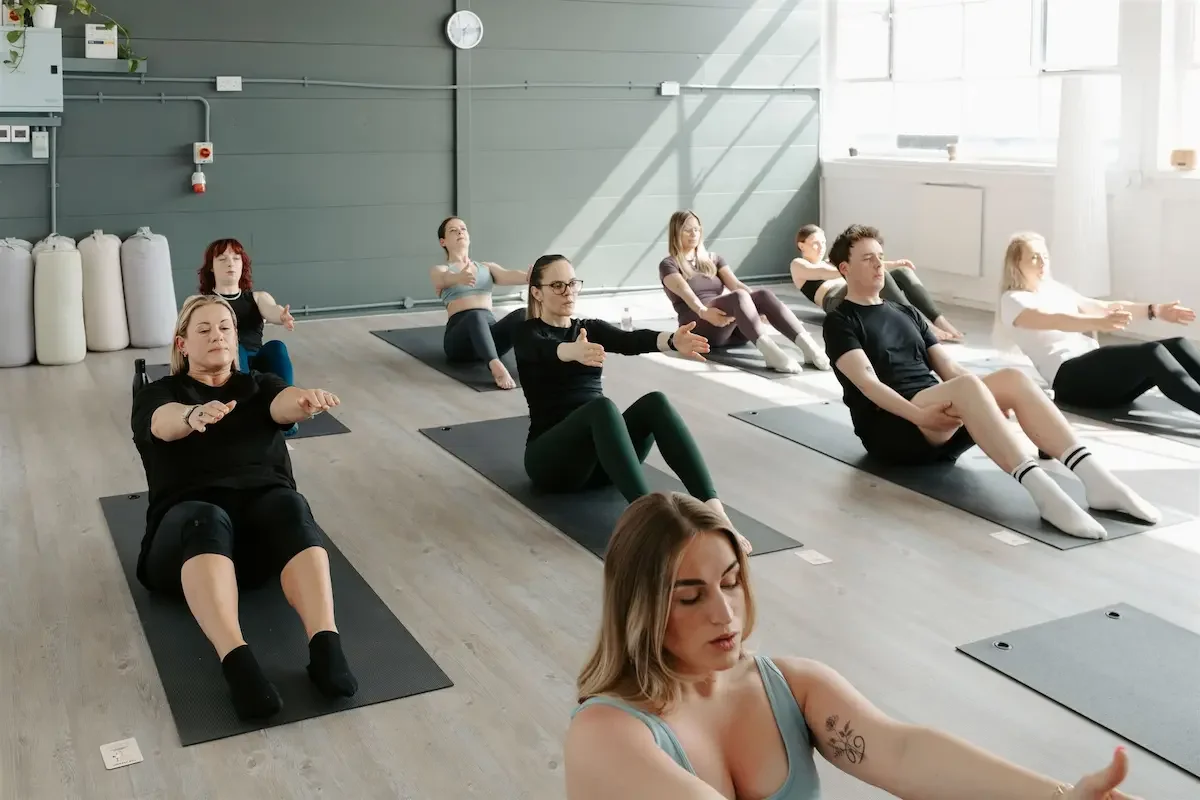 Group of students preparing for a core-strengthening yoga movement in a bright yoga studio in Glasgow's East End during a Core Yoga class.