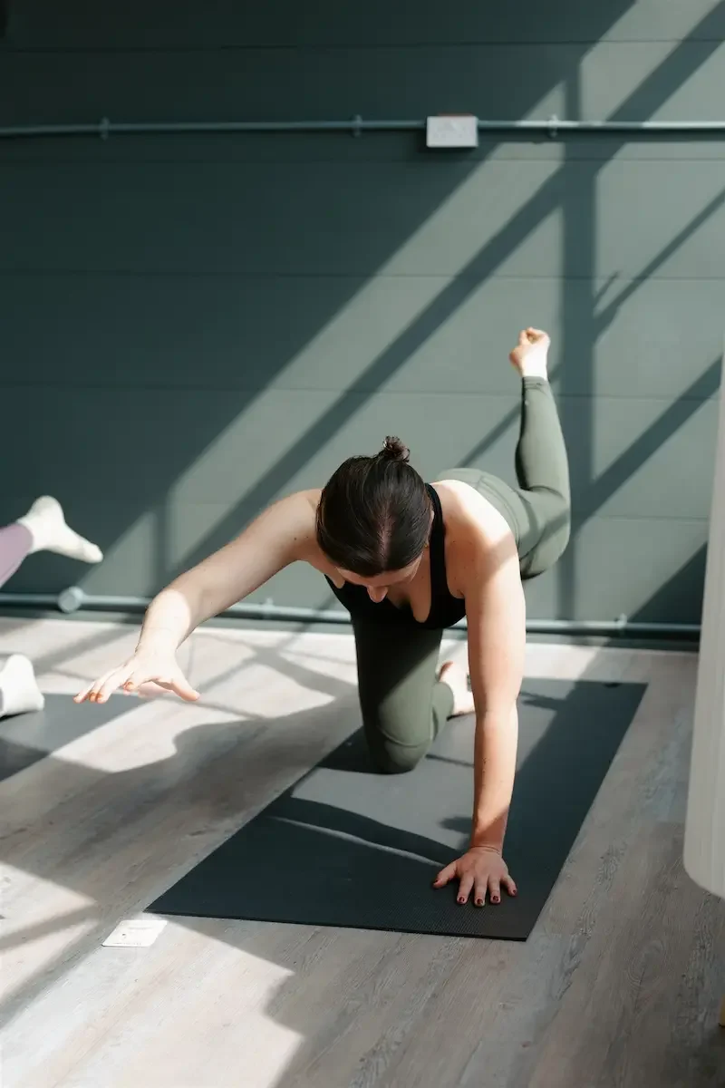Woman performing a glute-strengthening Pilates exercise on all fours in a bright, modern East End Pilates studio in Glasgow during a Pilates Sculpt class.
