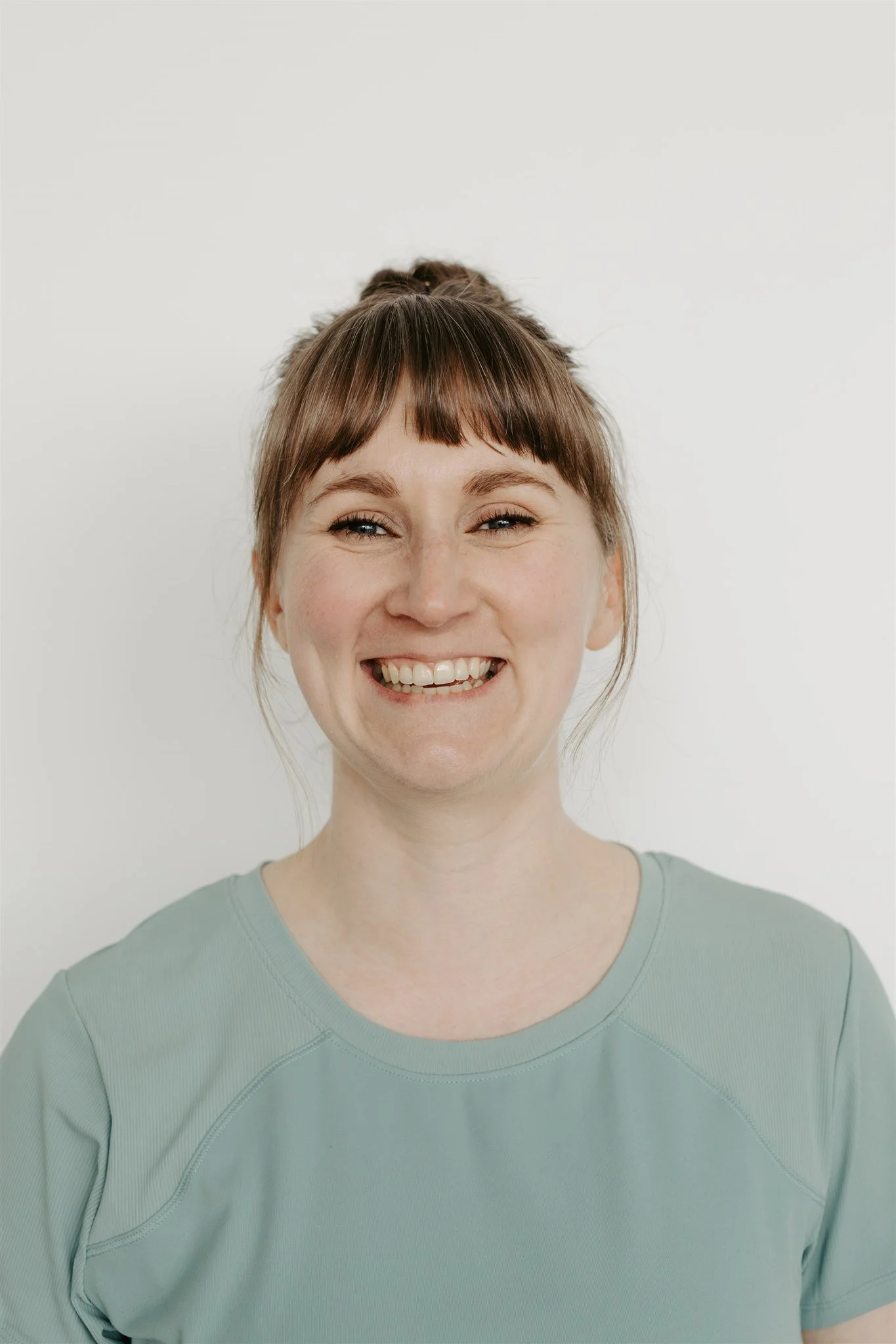 Image of Jennifer Mullan, glasgow pilates teacher,smiling with her hair in a bun, wearing a teal tshirt