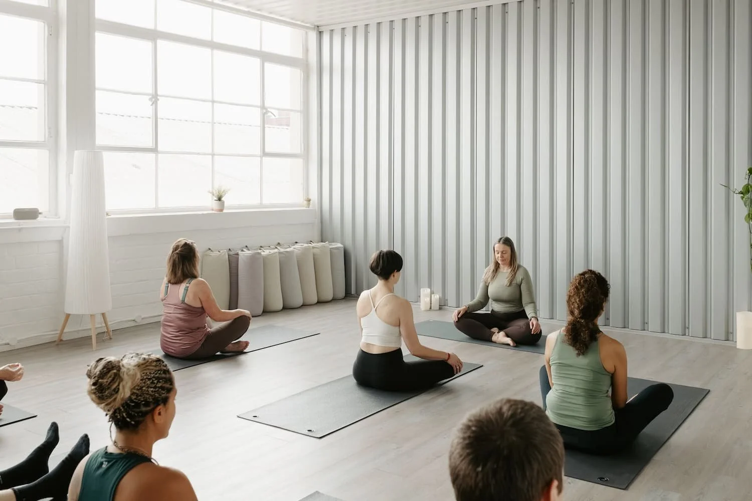 Yoga and Pilates teachers sitting cross-legged at the start of a class session during a teacher mentoring programme in Glasgow.
