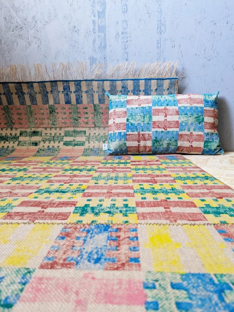 studio interior scene with rug on floor with hand printed check and stripe pattern on cushion in bold summer colours with rustic effect