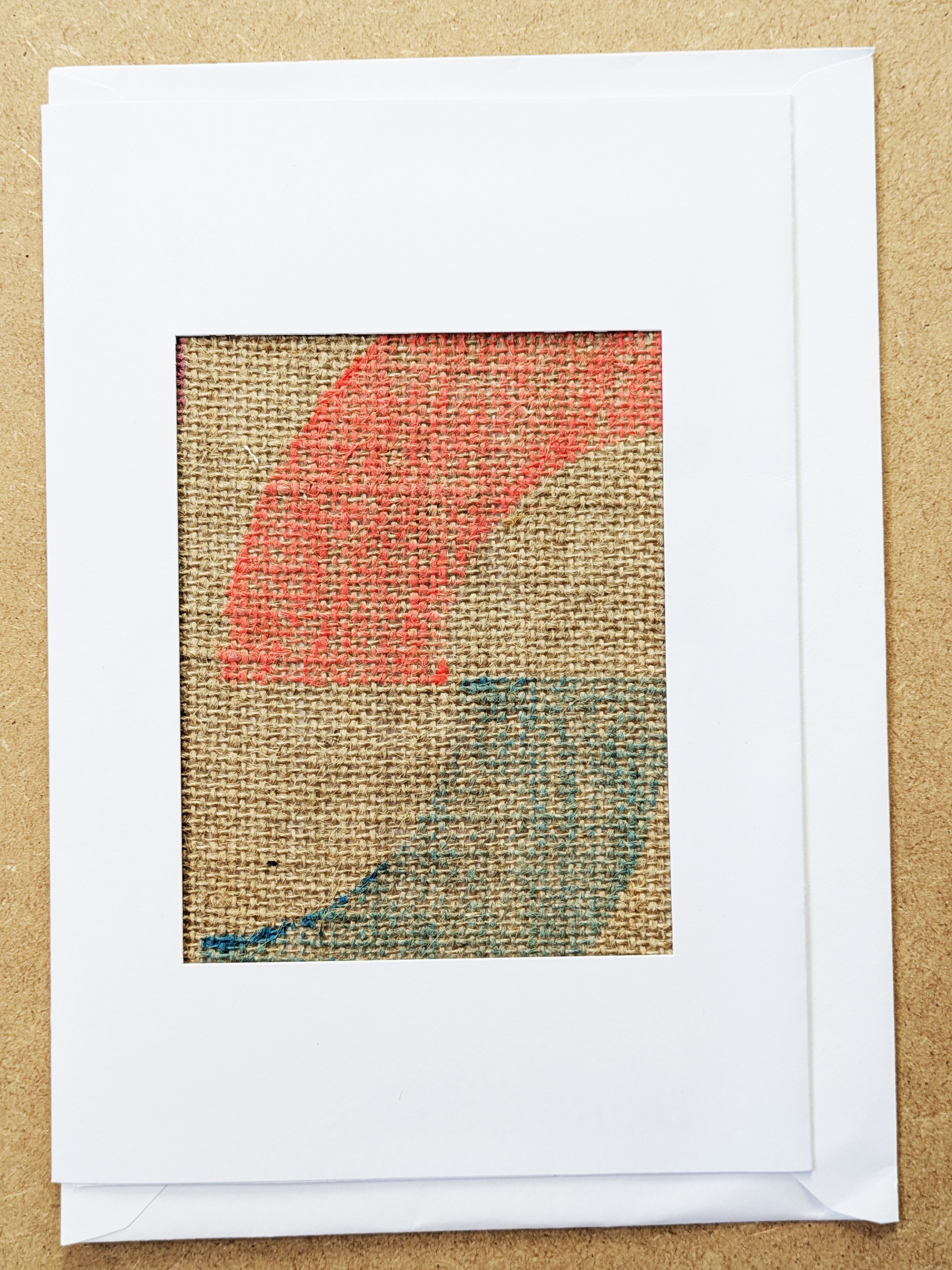 neon red and bright blue circular print on jute fabric framed in white postcard frame and white envelope