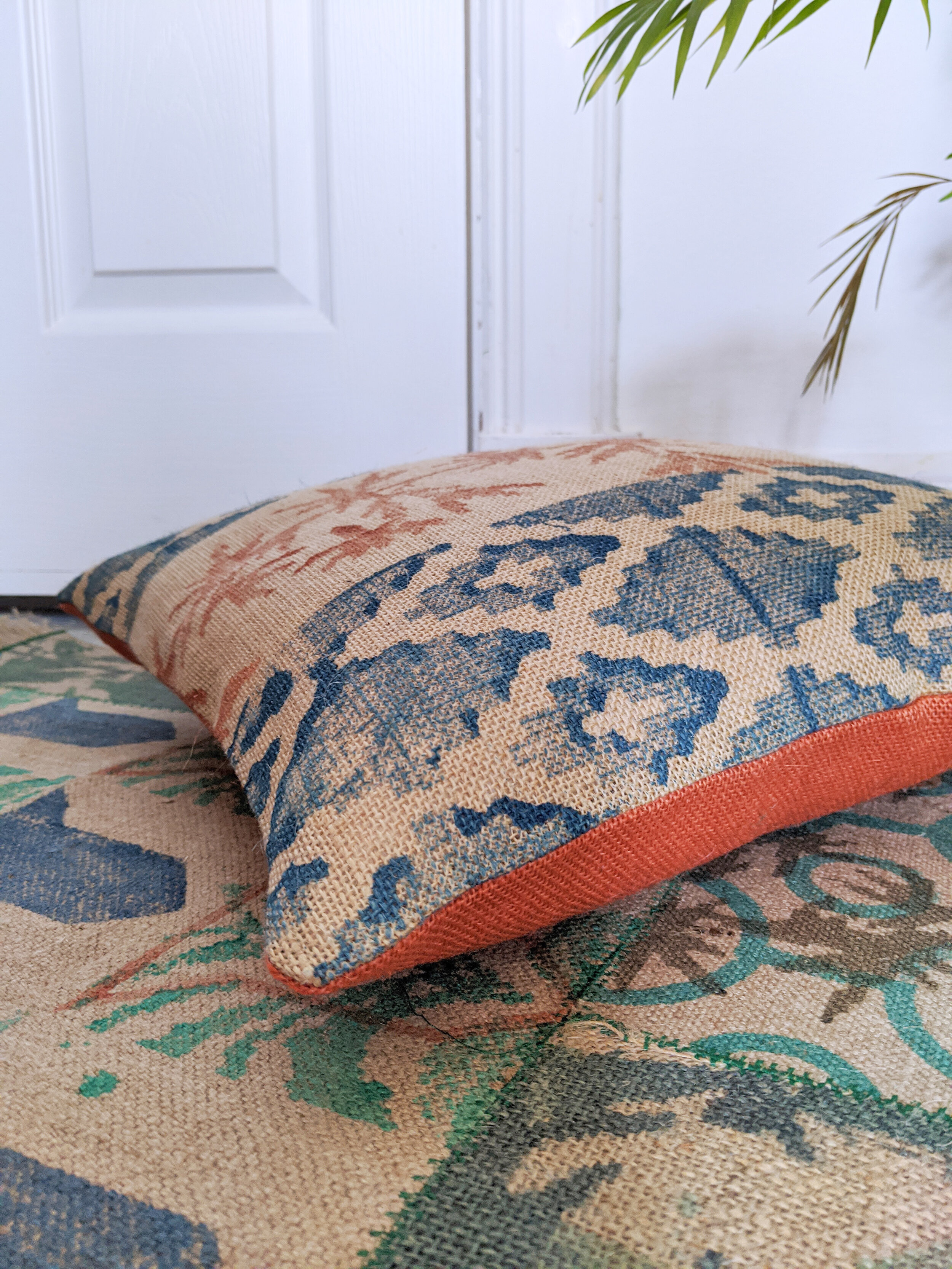 NOMÁD handmade jute cushion with boho print with orange back on green palm leaf rug