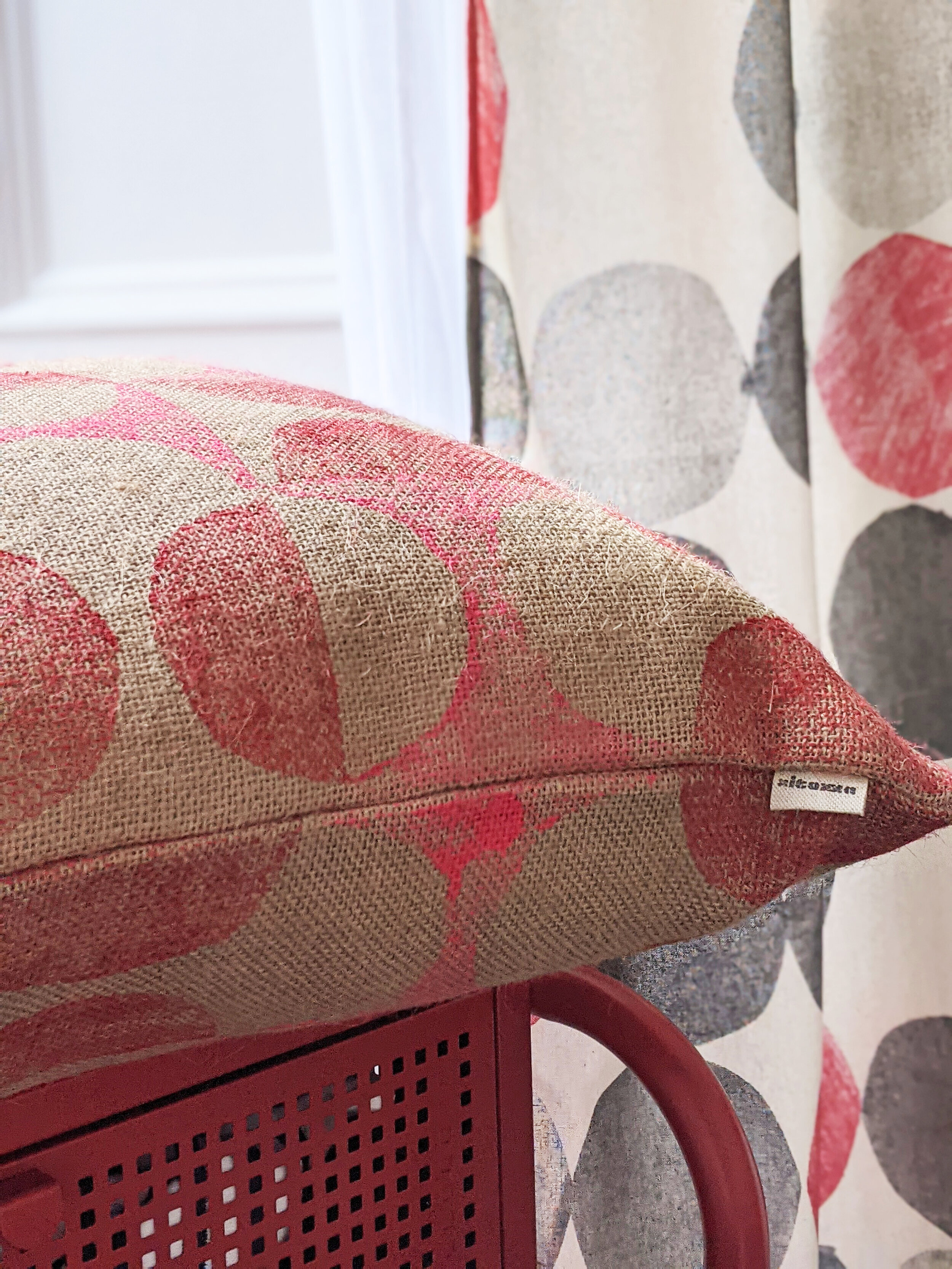 interior scene with 1960s inspired circular block printed abstract geometric curtain and cushion in red pattern