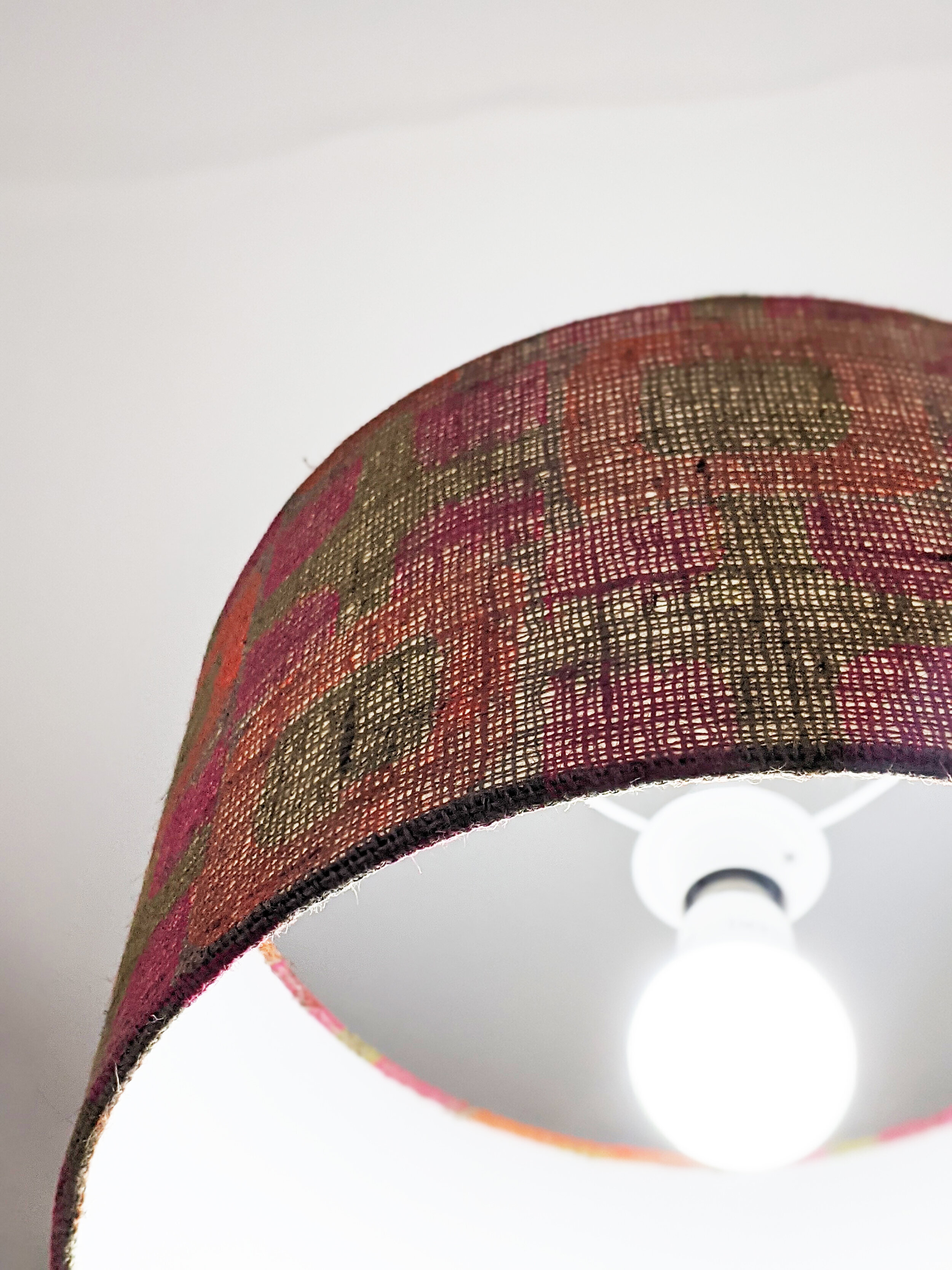 close-up detail of illuminated light on hessian lampshade in bright colourful geometric pattern
