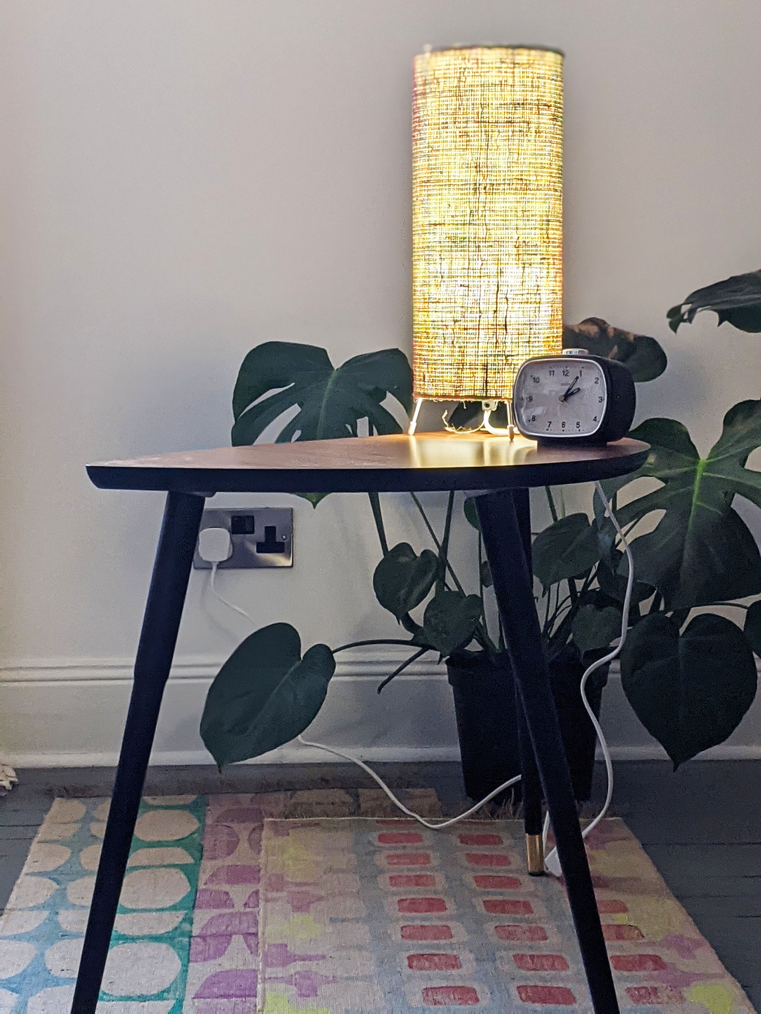 retro interior scene with houseplant and small table lamp, clock and colourful rugs