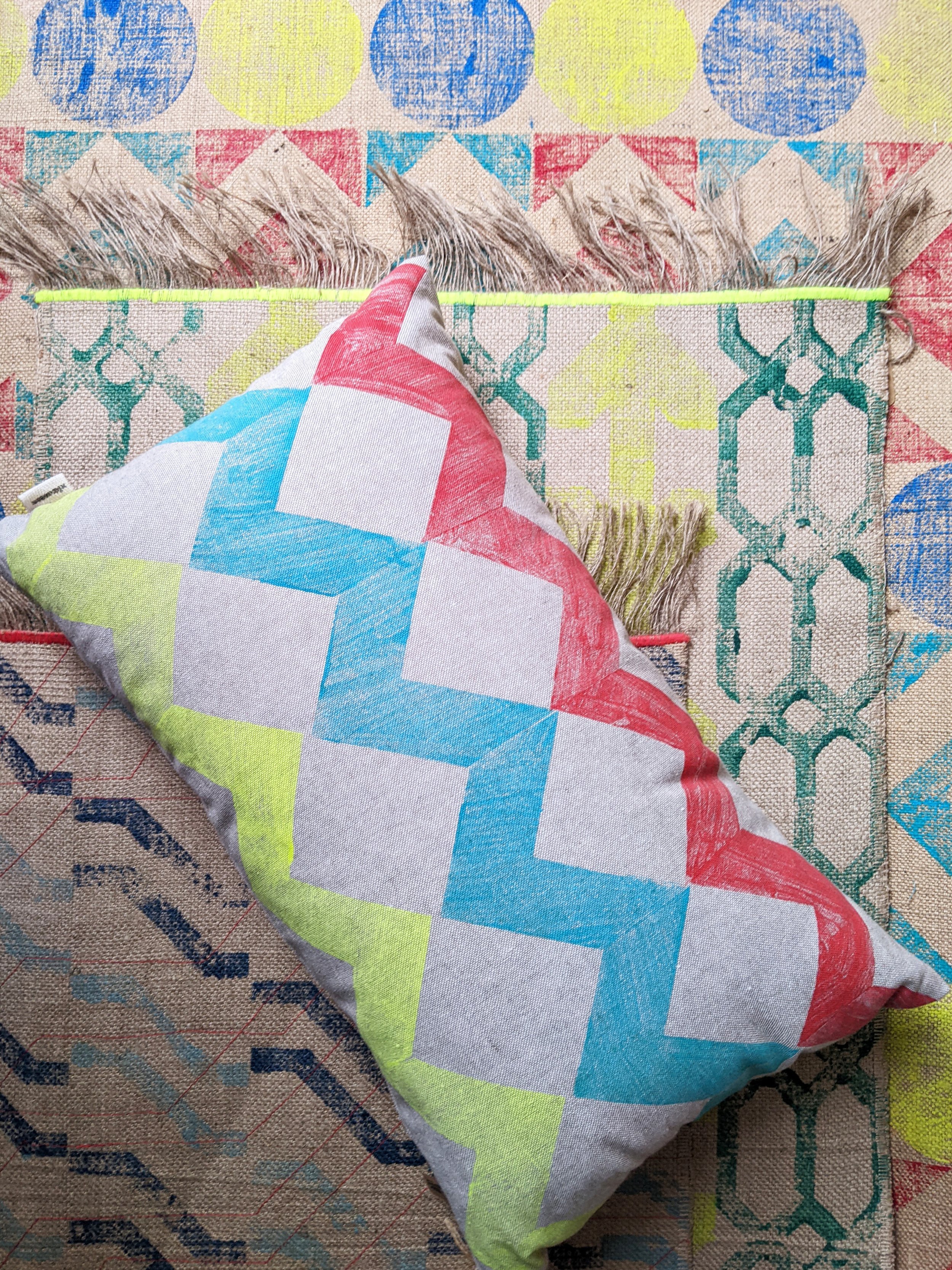 colourful interior scene with cushion with zigzag geometric print on a layer of colourful printed rugs on floor