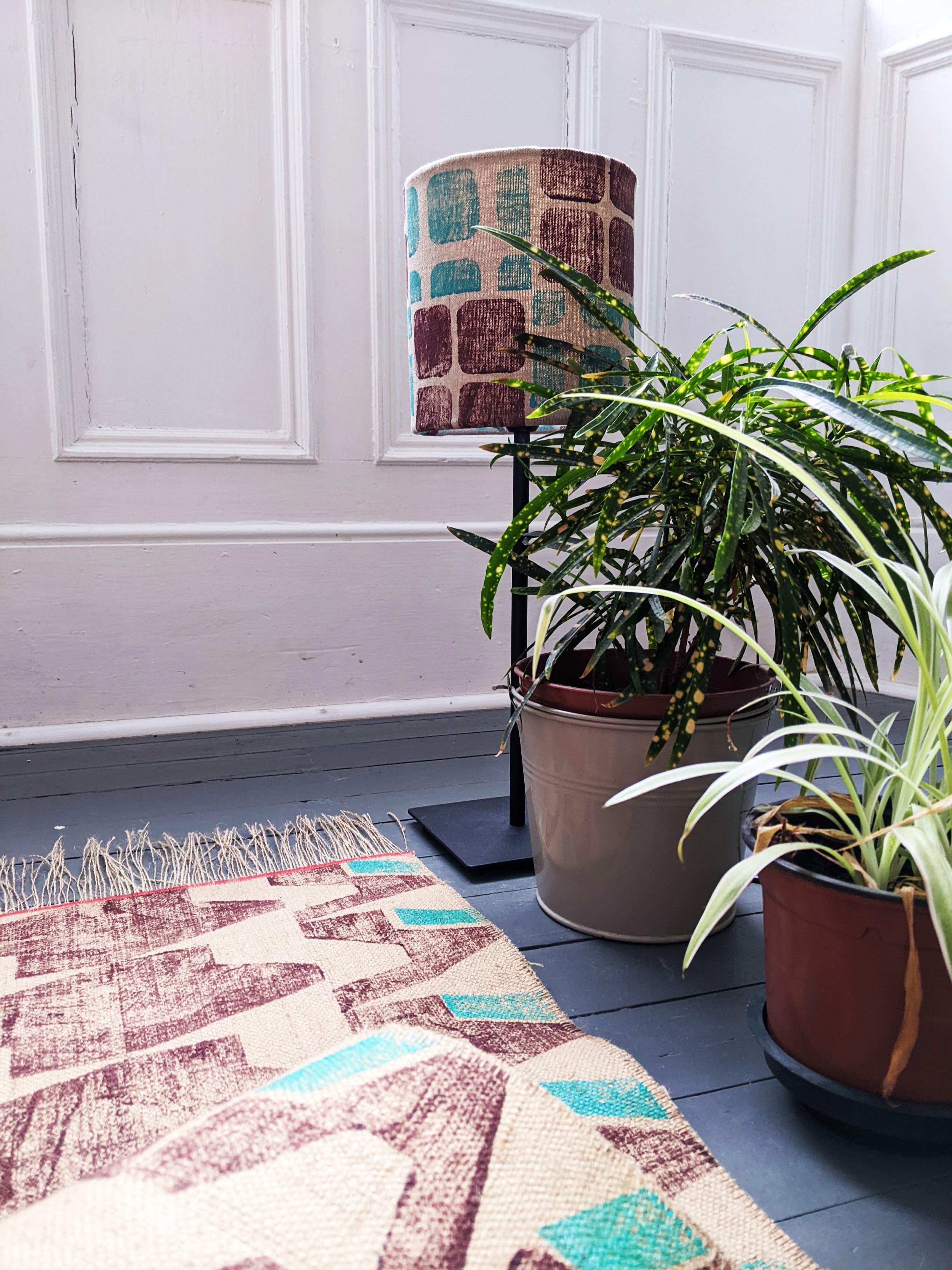 modern interior scene with small lamp in corner and geometric, brutalism-inspired print on lampshade and rug with houseplants on floor