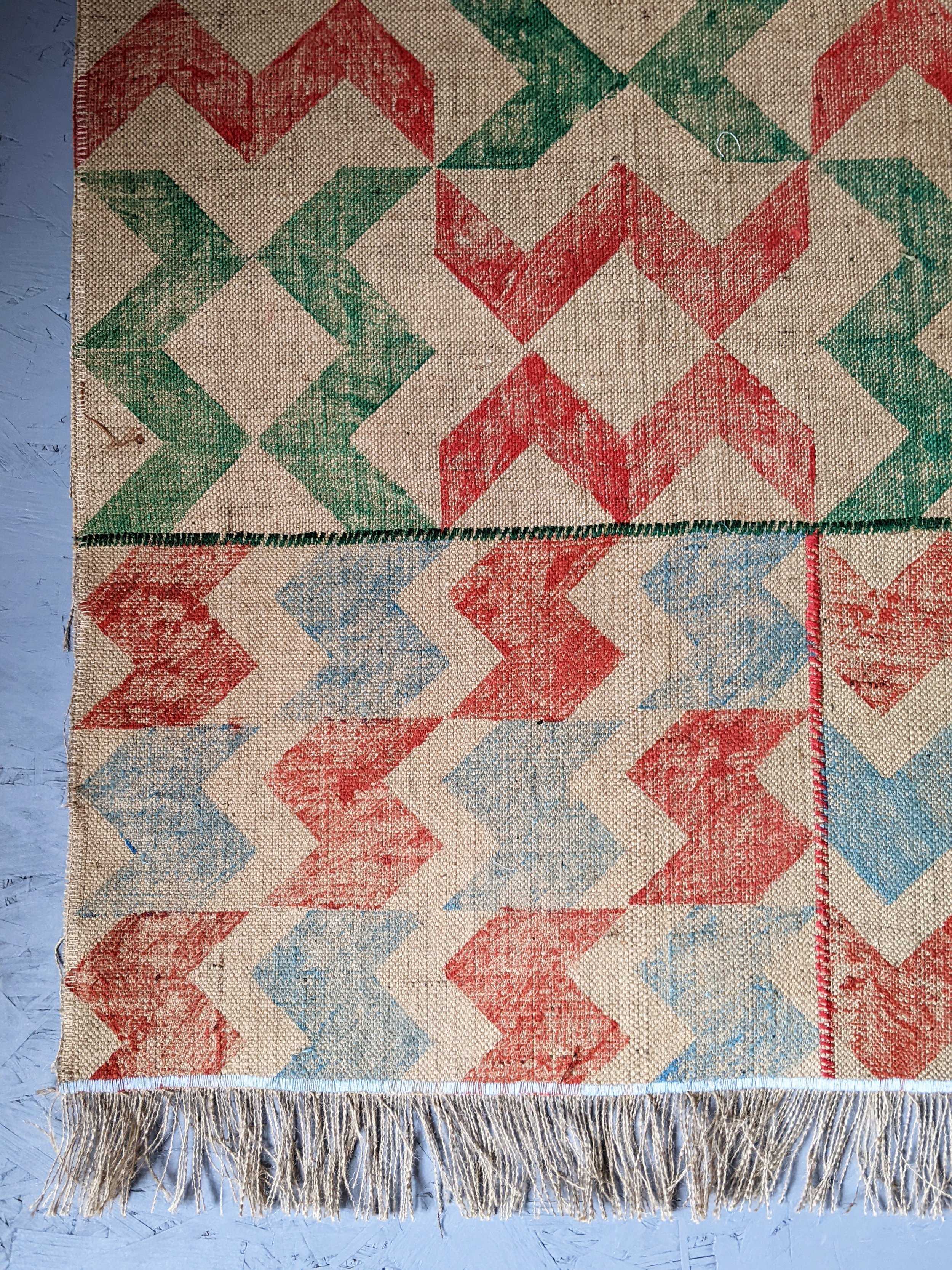 close-up details of stitched and printed panels of abstract zigzag striped jute rug in red and green