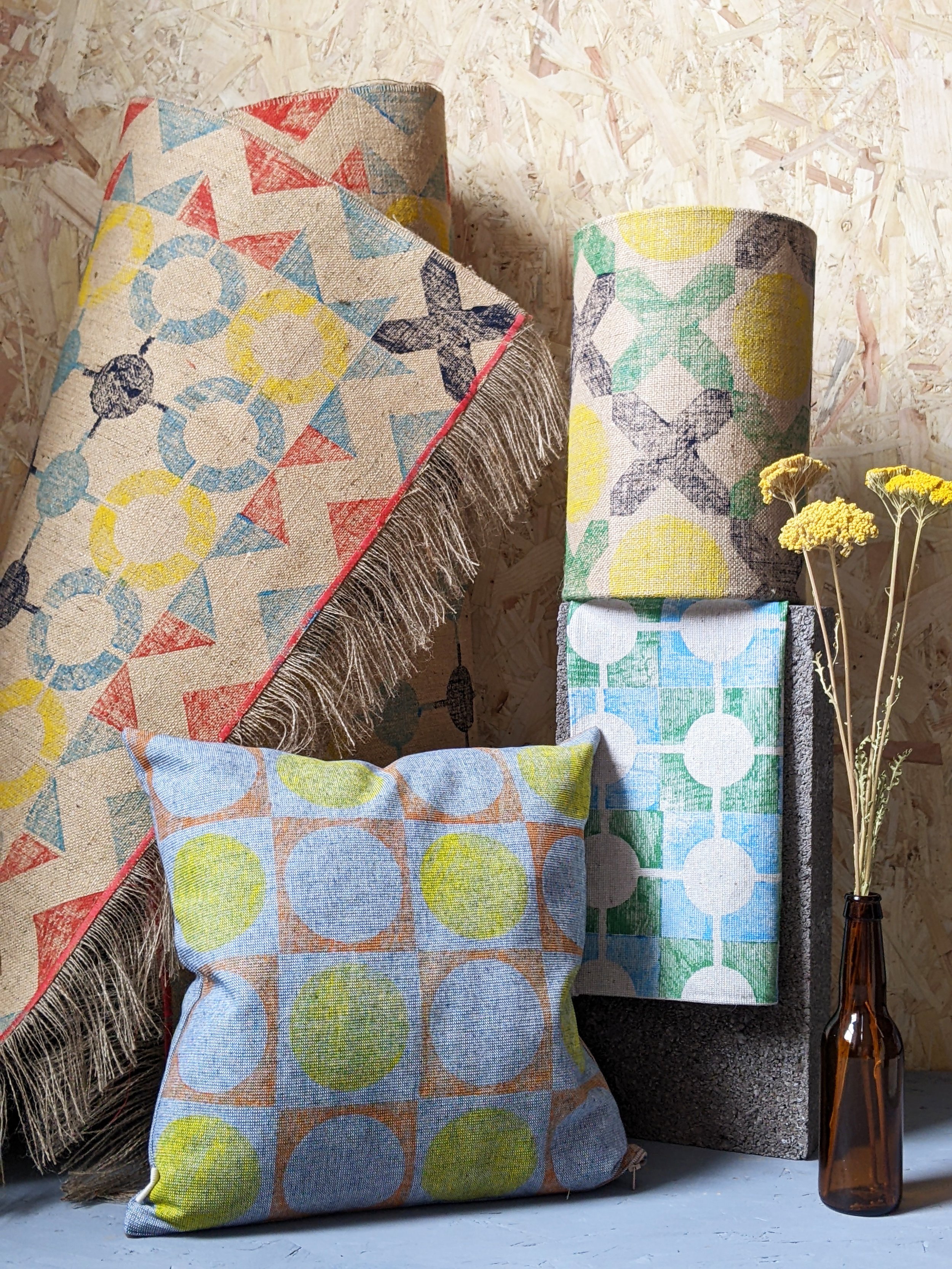 studio scene with block printed homewares display, rolled up nautical inspired rug and colourful lampshades and cushions in abstract geometric patterns