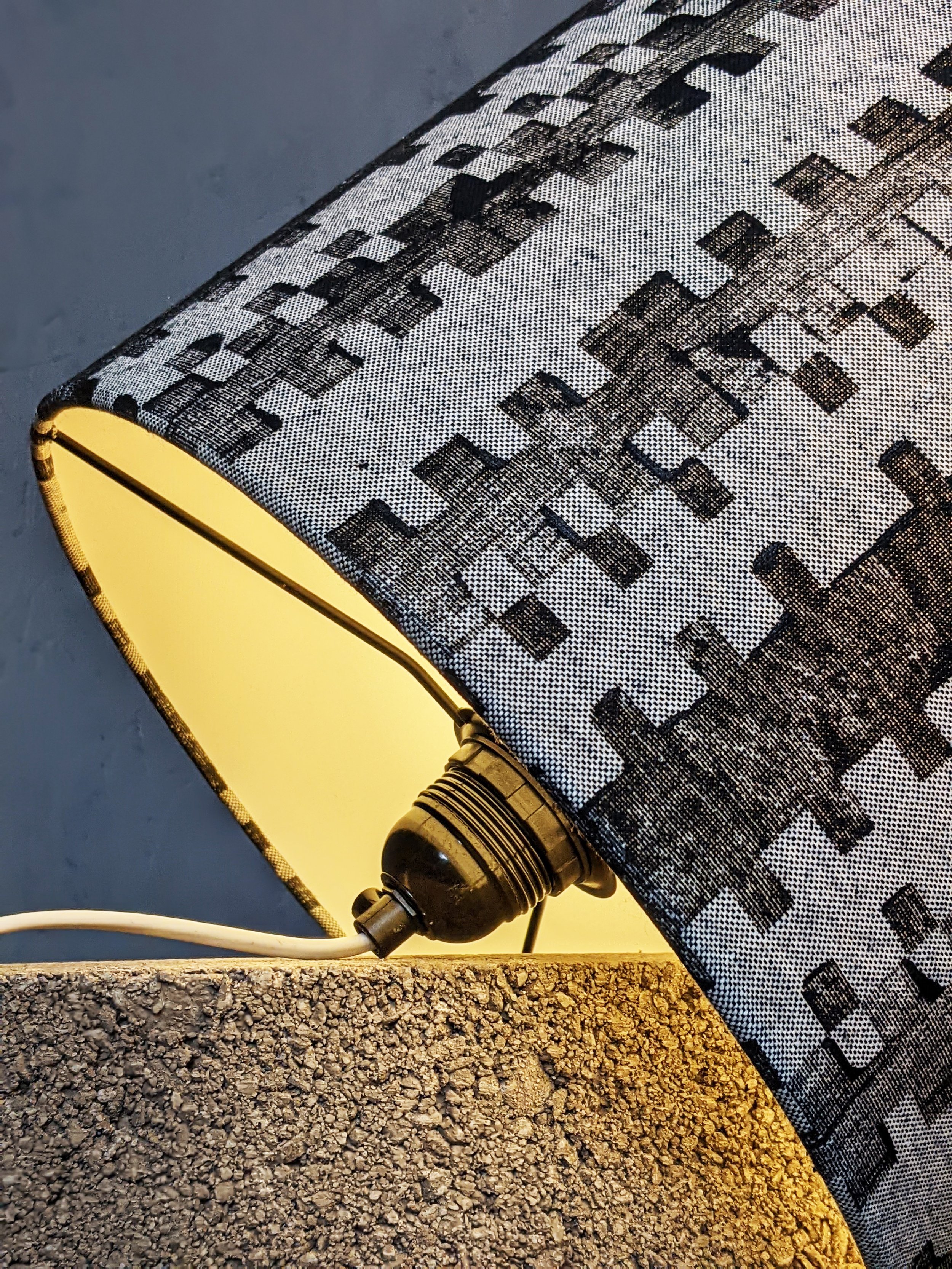 close-up detail of black hand printed pattern on woven fabric on lampshade with black frames and concrete block in brutalism inspired scene