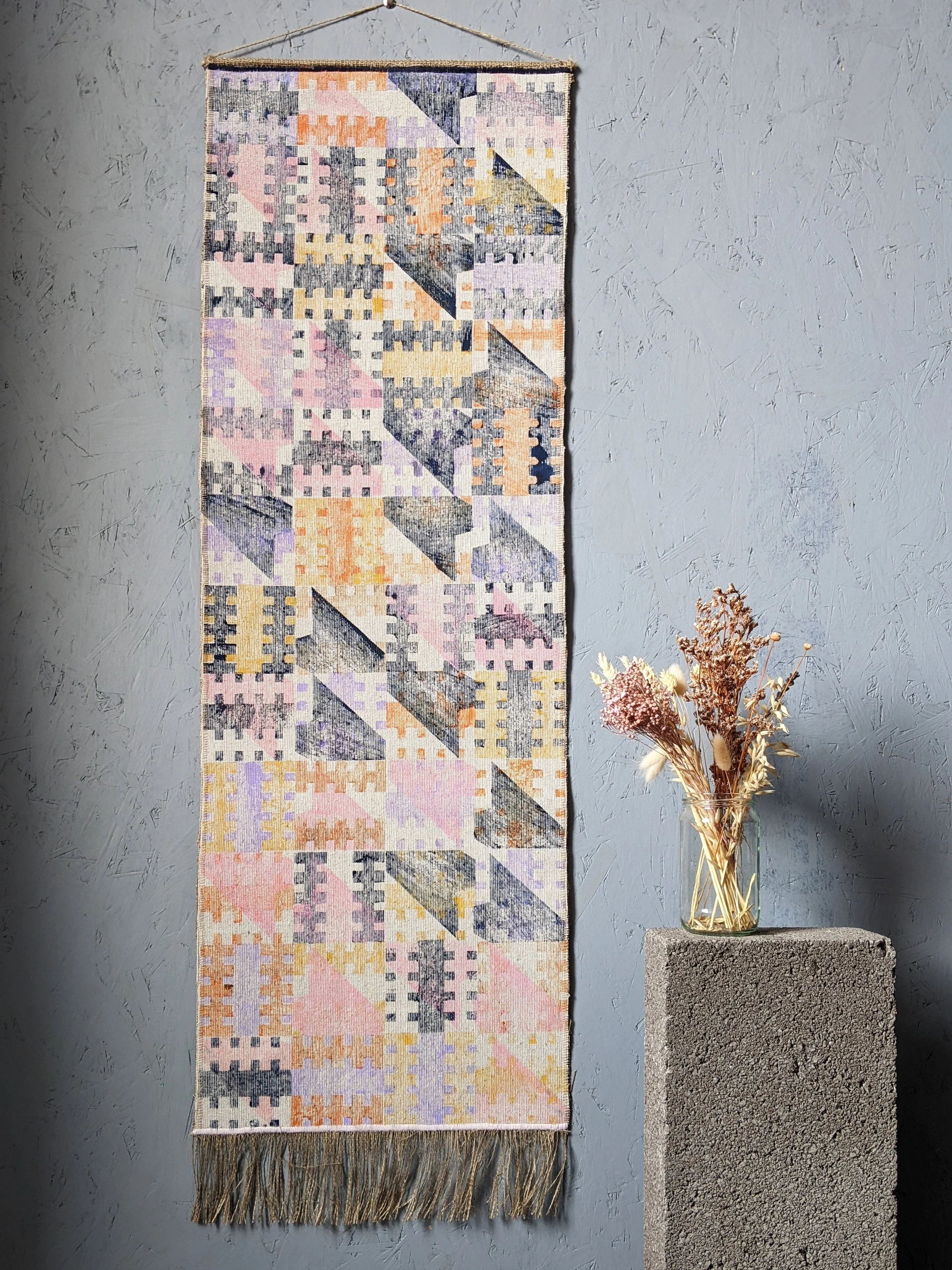 abstract architectural wall hanging on grey studio wall with flowers