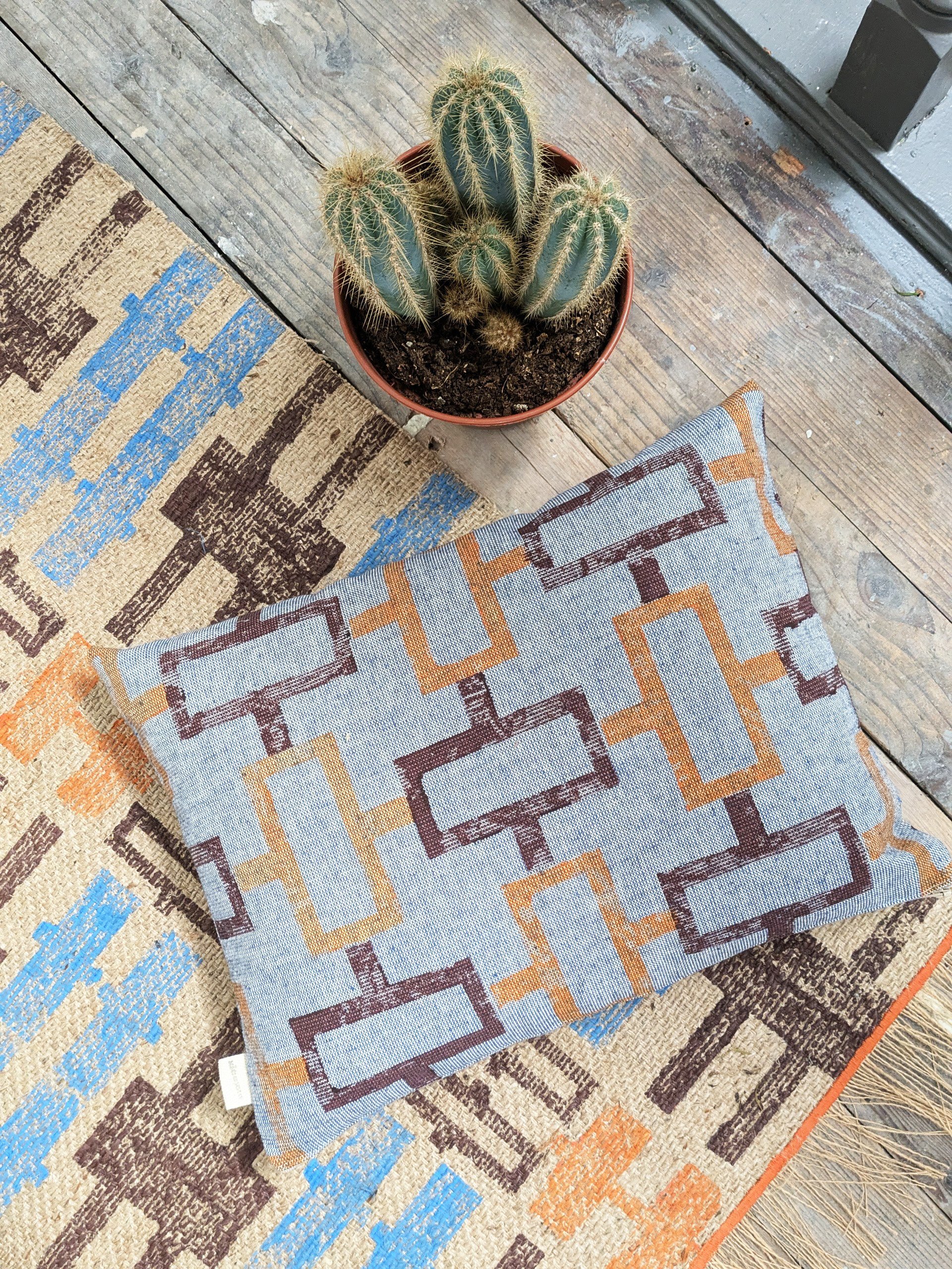 simple cushion design on floor with exotic jute rug in abstract, geometric print and maroon and orange colours