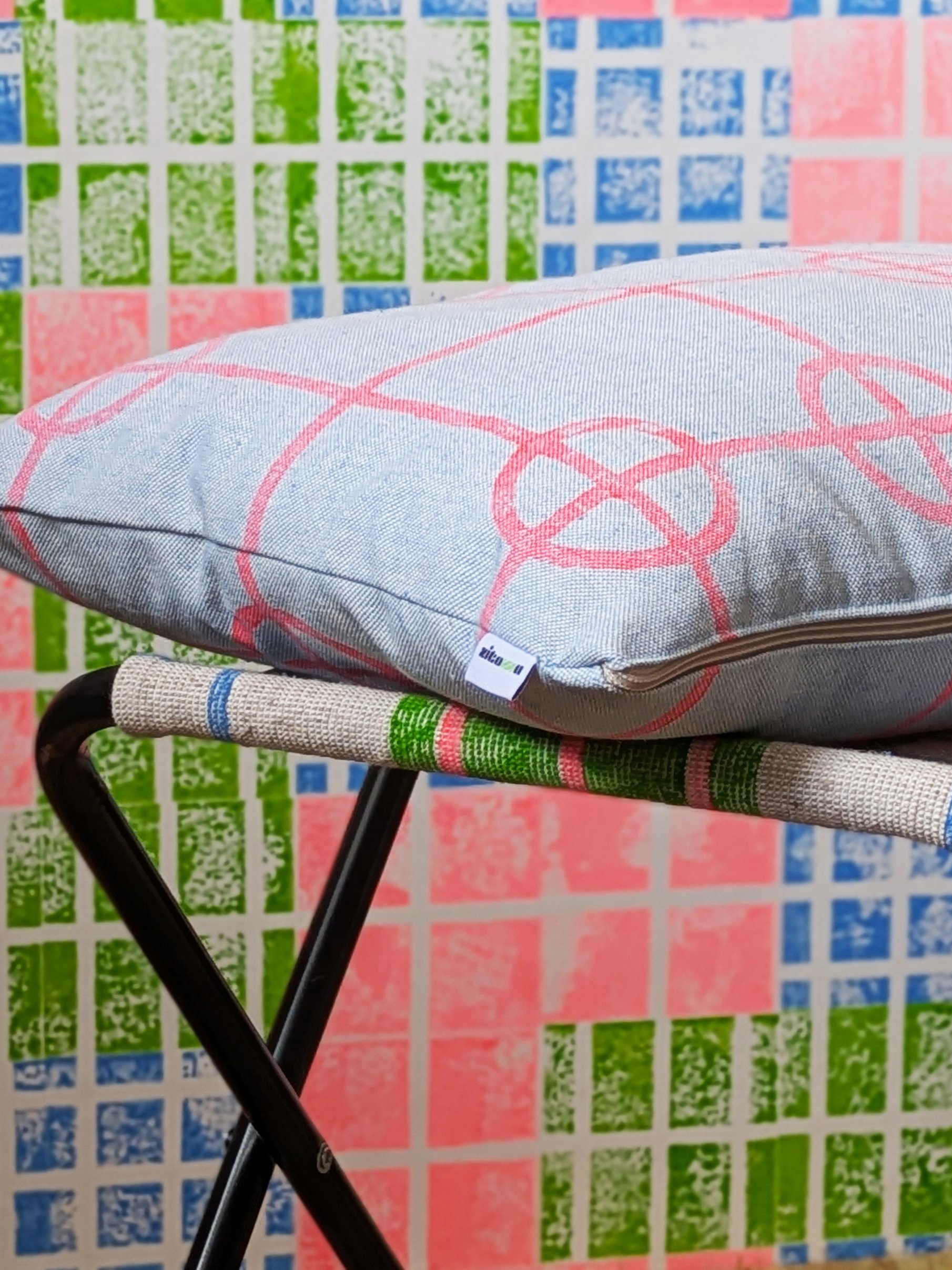 close-up detail of small rectangular cushion printed in neon red on blue fabric in an industrial-inspired simple grid pattern