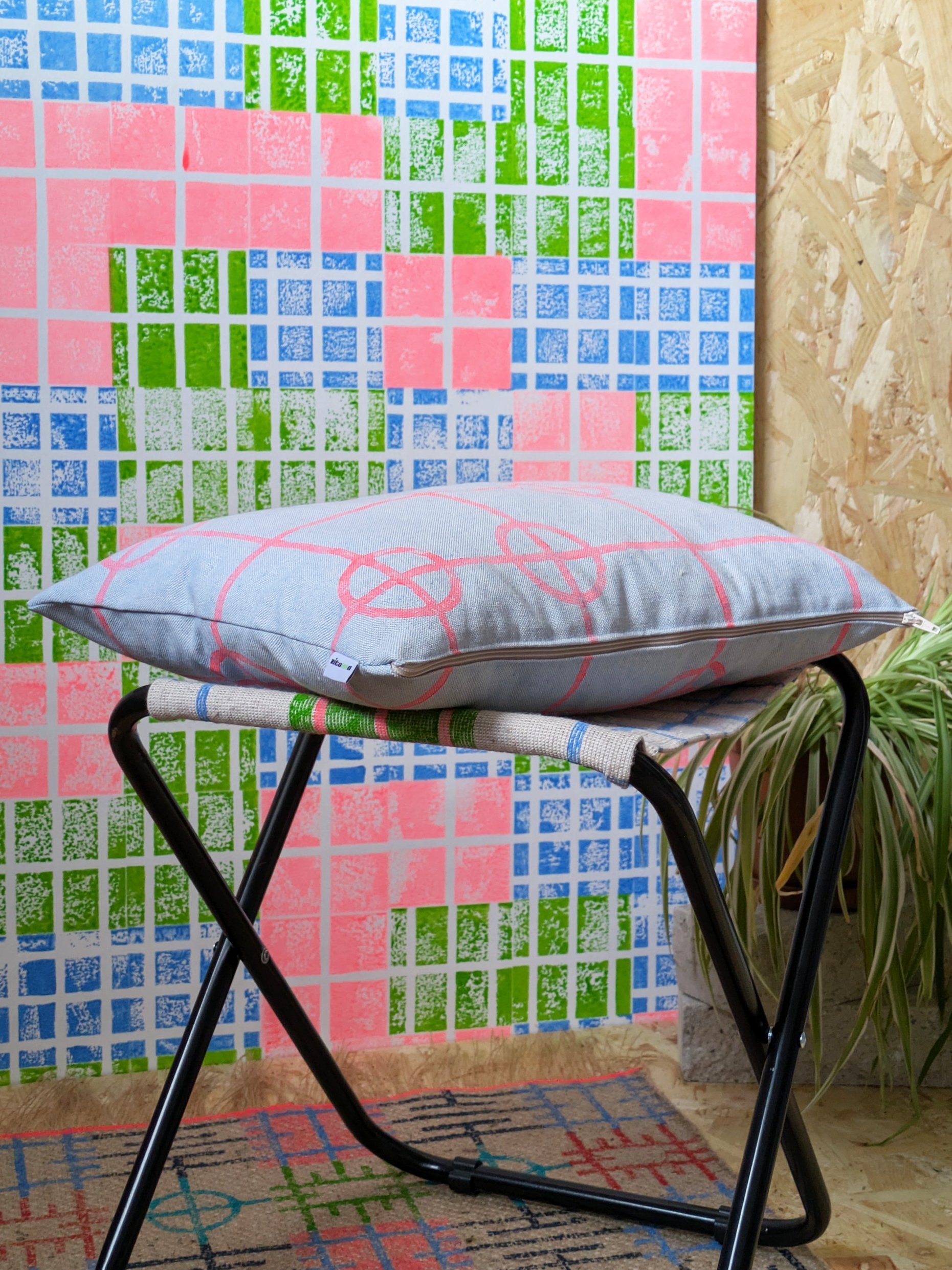 bright bold interior scene with fun wallpaper in grid print and small cushion with simple print in foreground