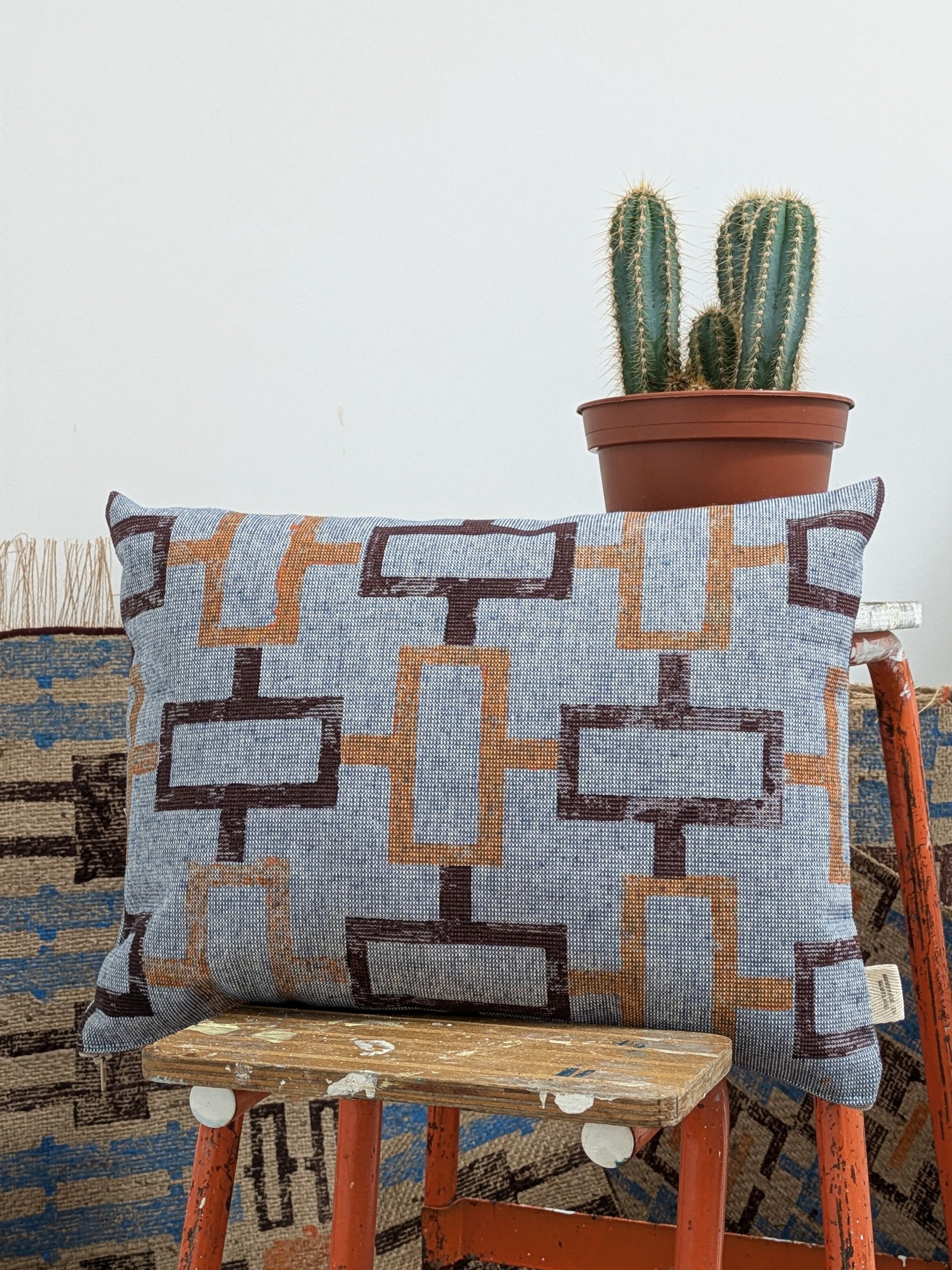small cushion with simple maroon and orange geometric print on denim-like cotton fabric and ethnic printed jute rugs