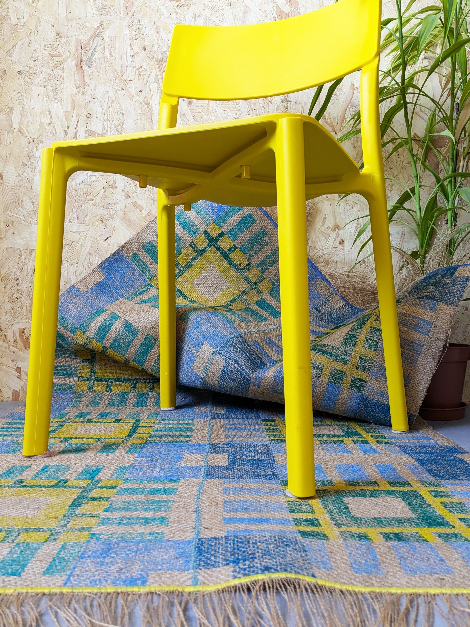 colourful studio scene with printed geometric jute rug in cool blue, green and yellow colours and yellow plastic chair