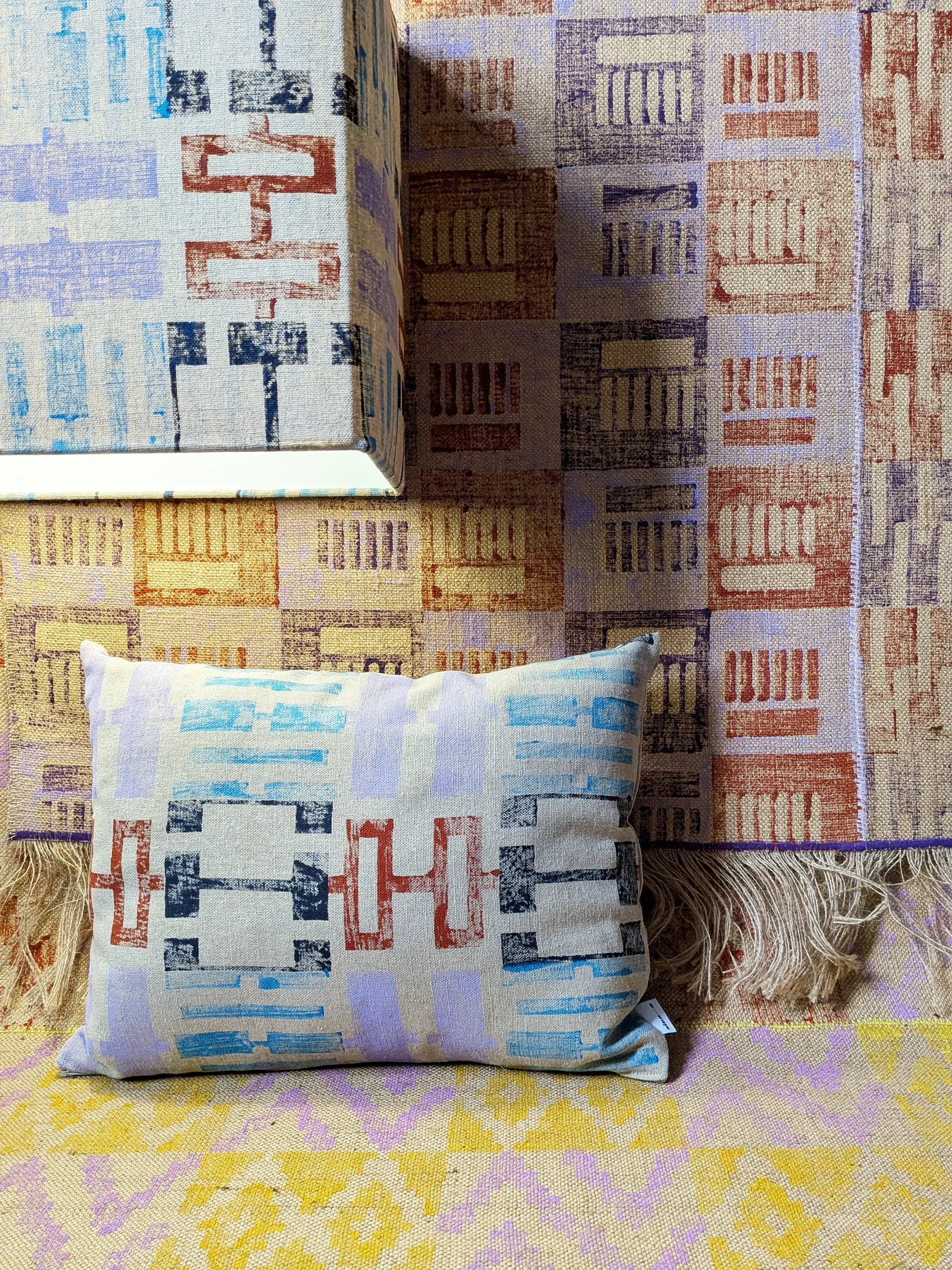 cosy studio scene with warm linen light and tactile rugs and cushion in warm pastel colours and architecture inspired geometric patterns